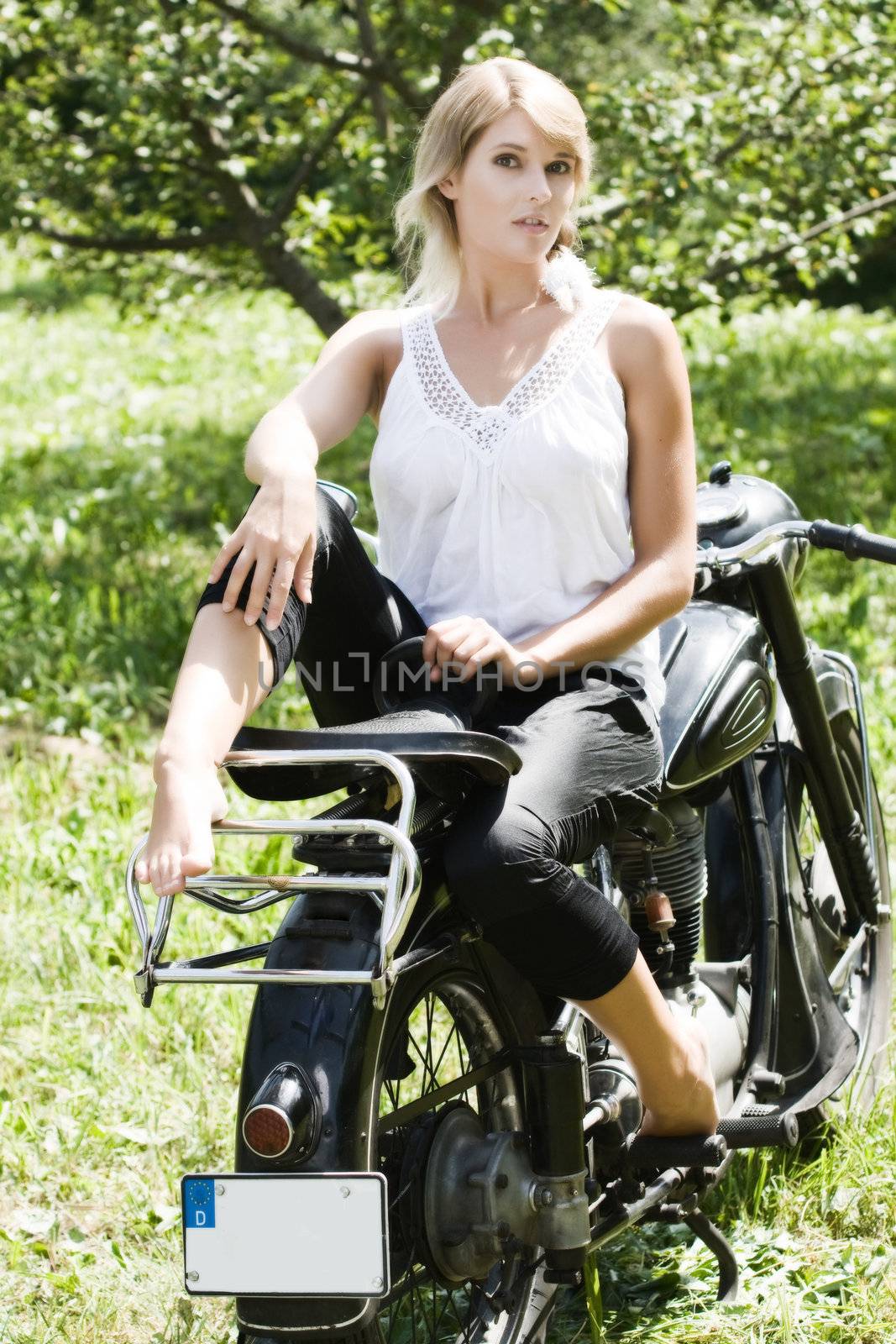 Fashionably dressed woman seated on an old motorcycle