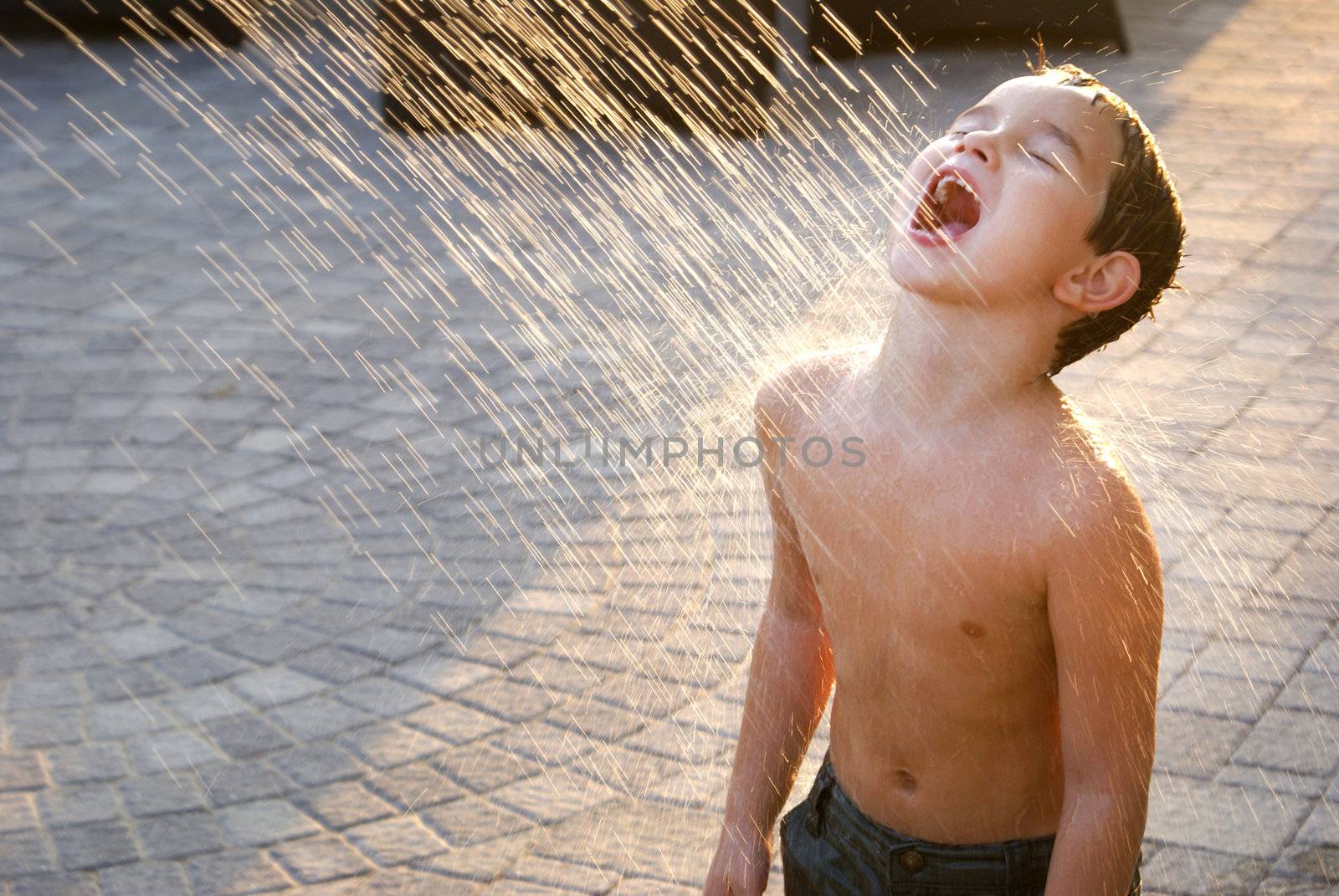 A six years old kid having water from the sprinkler.