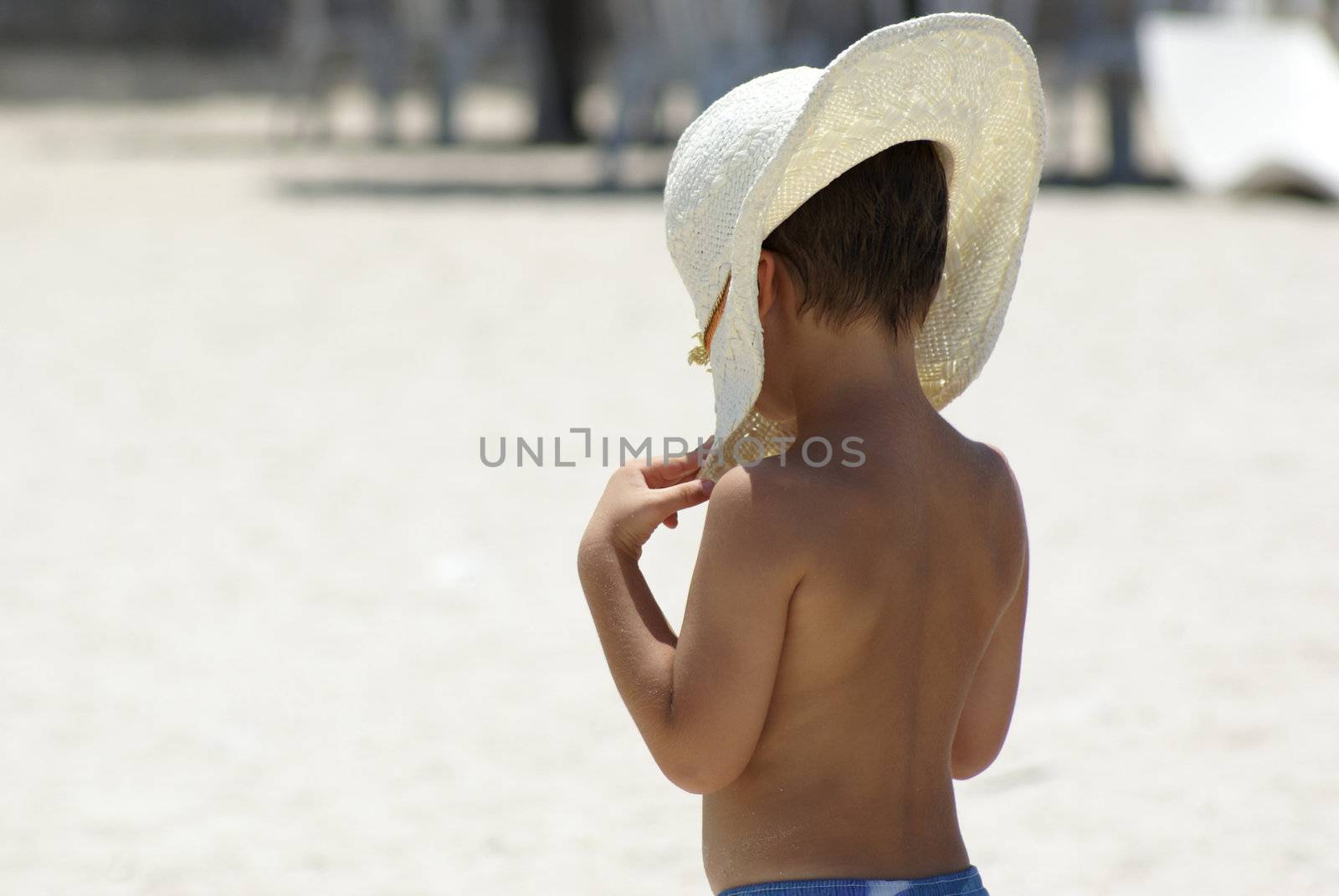 A boy protecting himself with sunshine with his mothers hat at the beach.