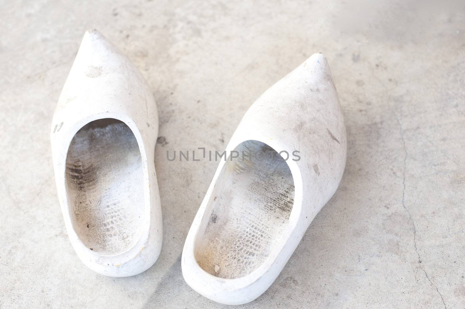 pair of undecorated white wooden clogs on a dirty concrete floor