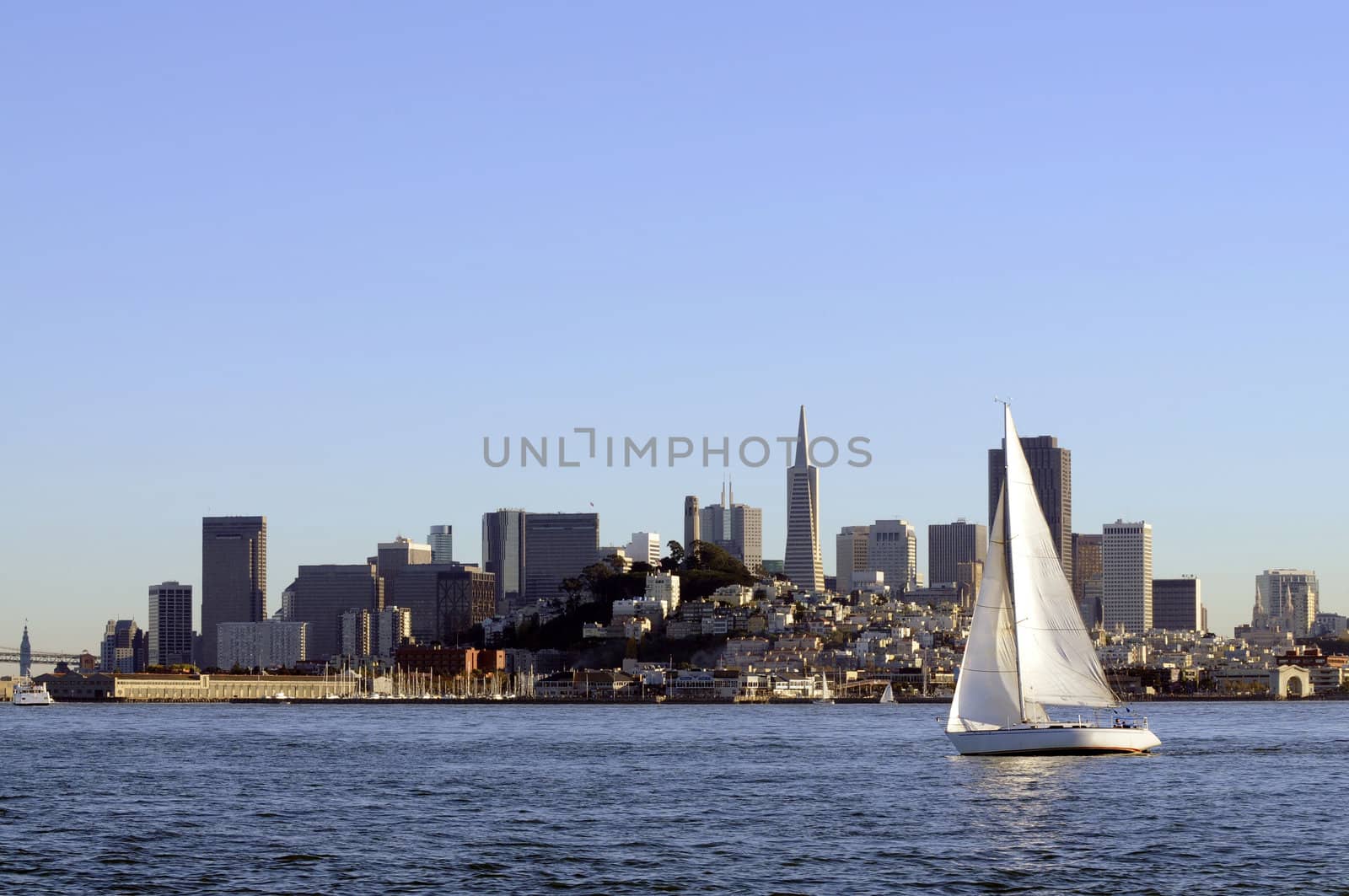 San Francisco Skyline at sunset coming into port, with a sailboat crossing the bow