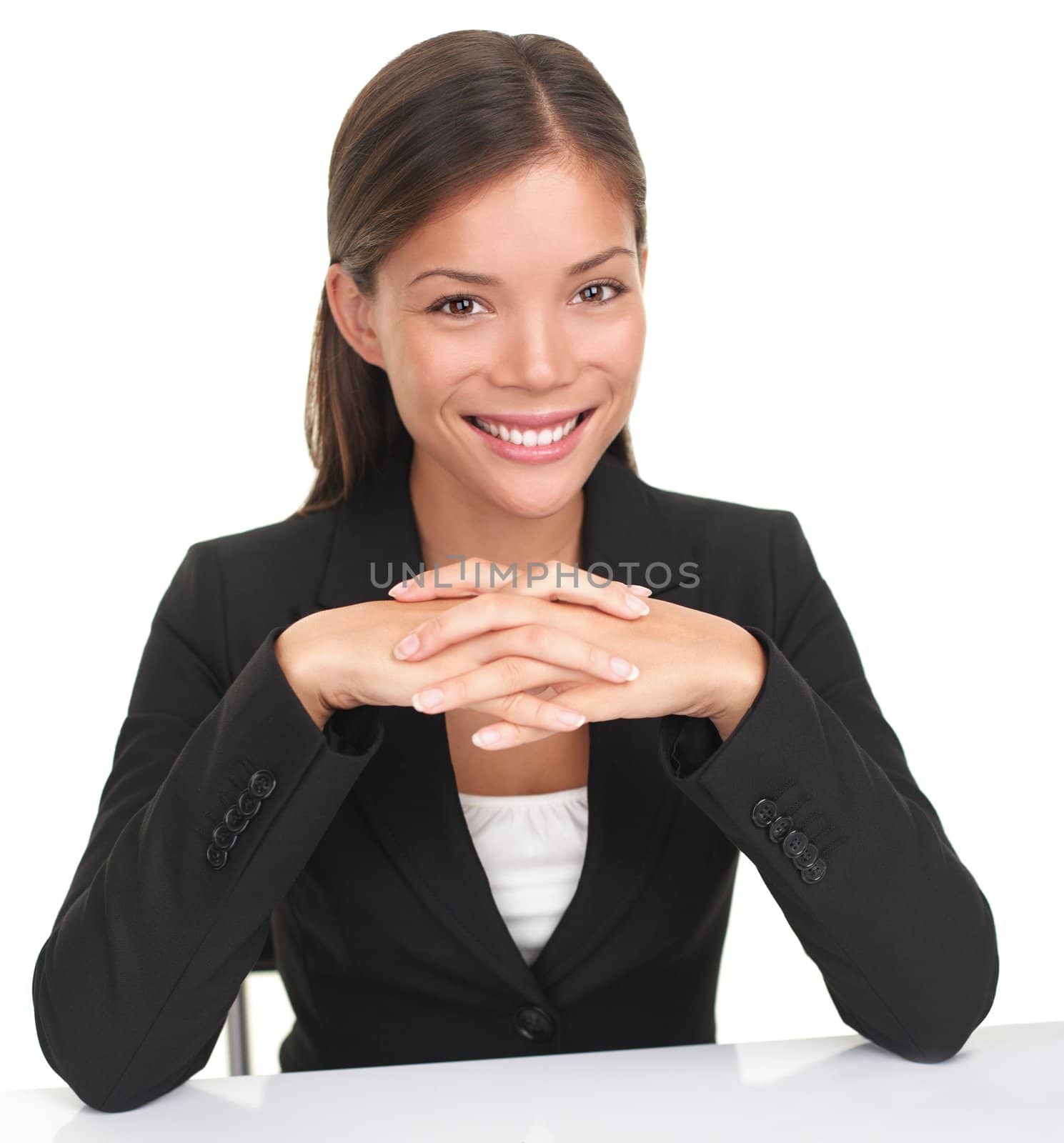 Business woman sitting at table smiling with hands folded. Young Caucasian Asian professional woman isolated on white background.