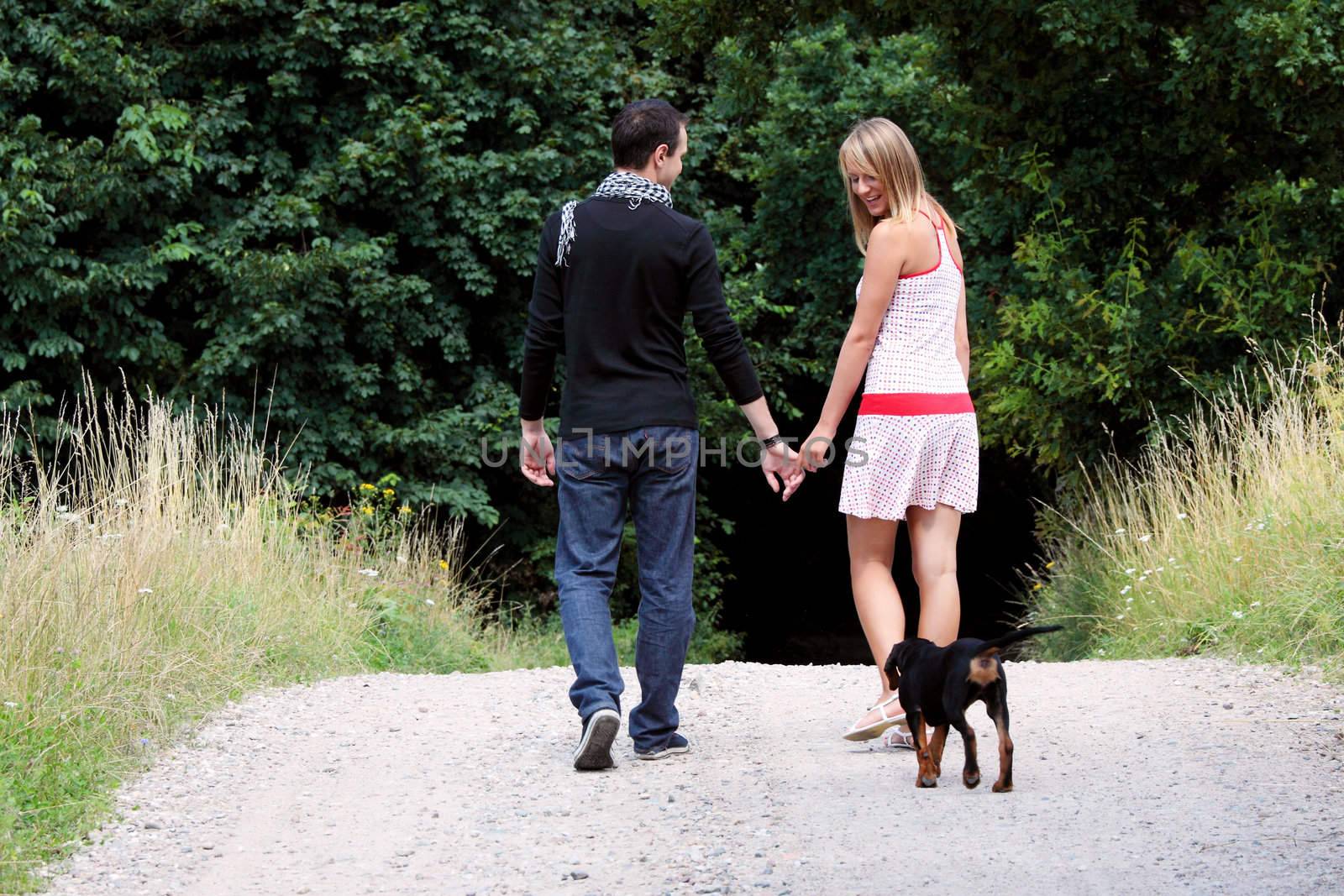 Young couple in meadow walking with dog.