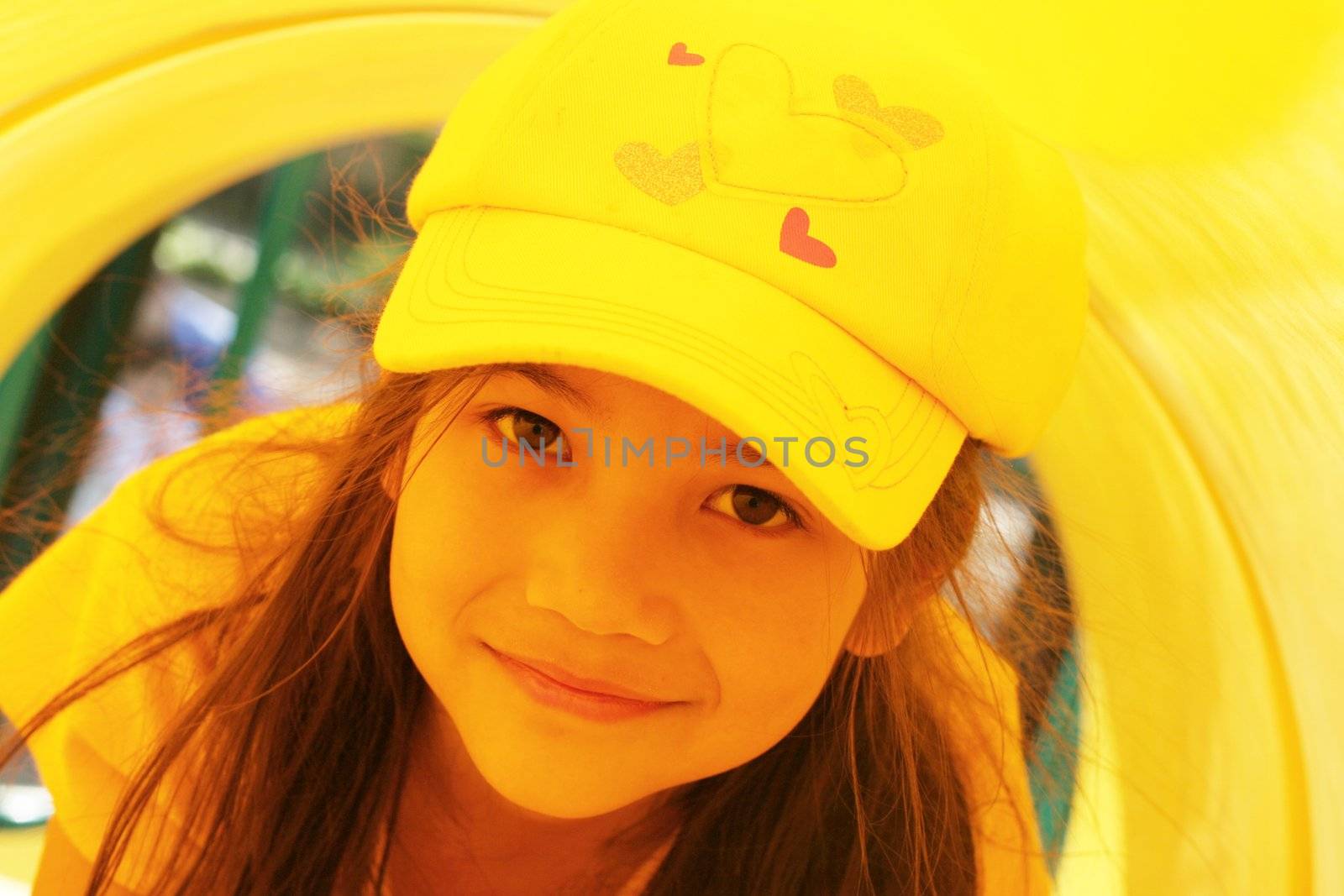 Beautiful little girl playing inside a yellow tube at playground