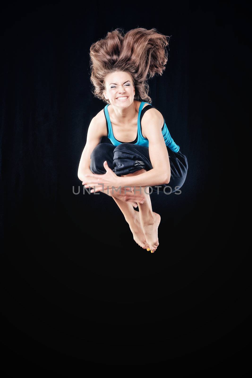 Young woman in tracksuit jumping on black background