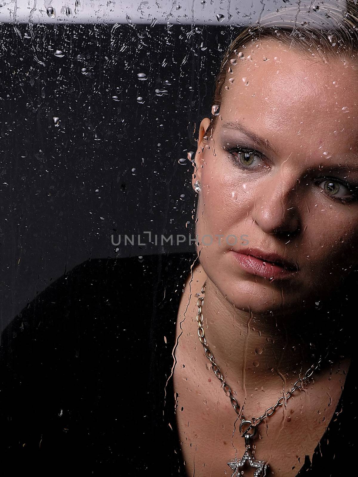 Womans face behind glass with rain drops