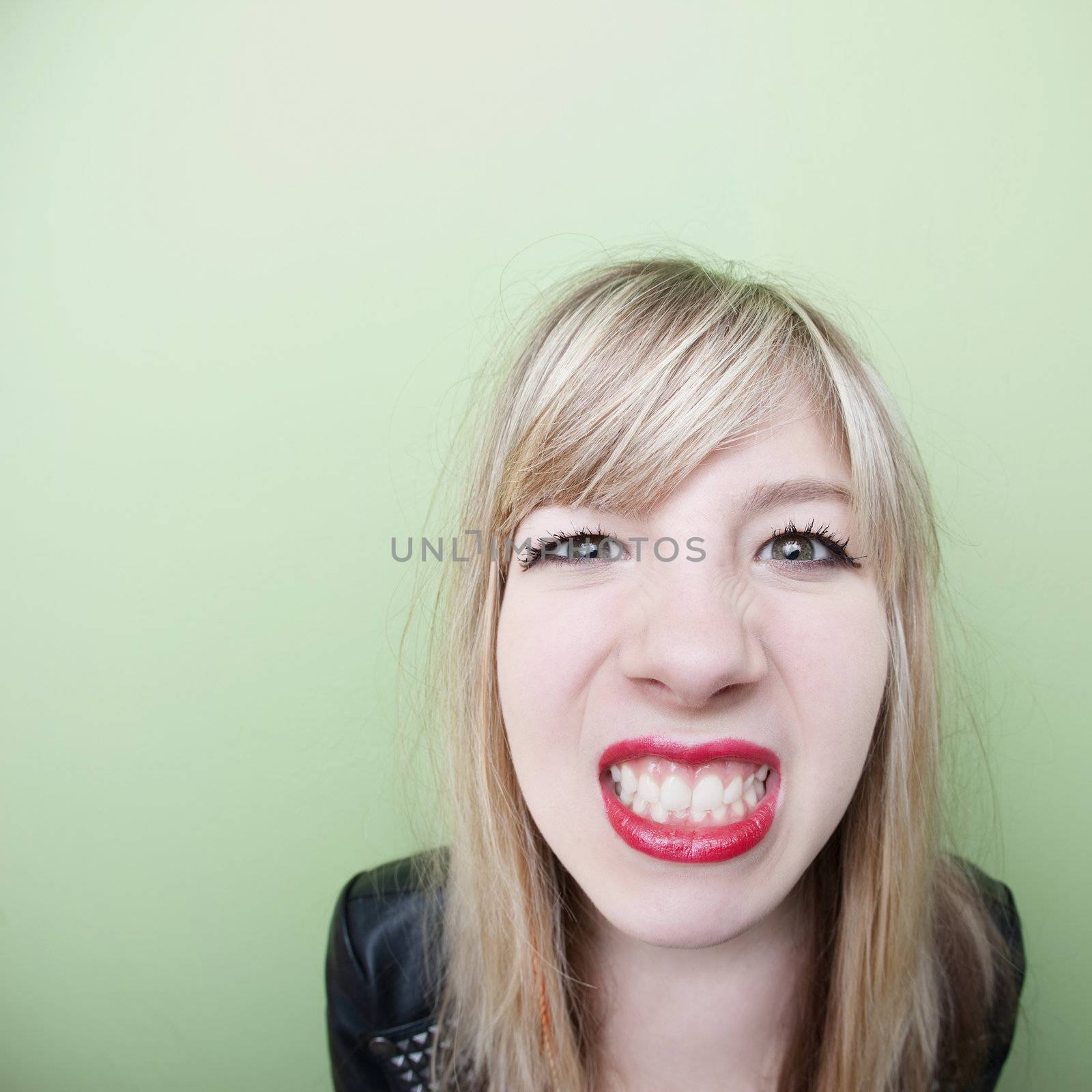 Young Caucasian lady clenches her teeth over green background