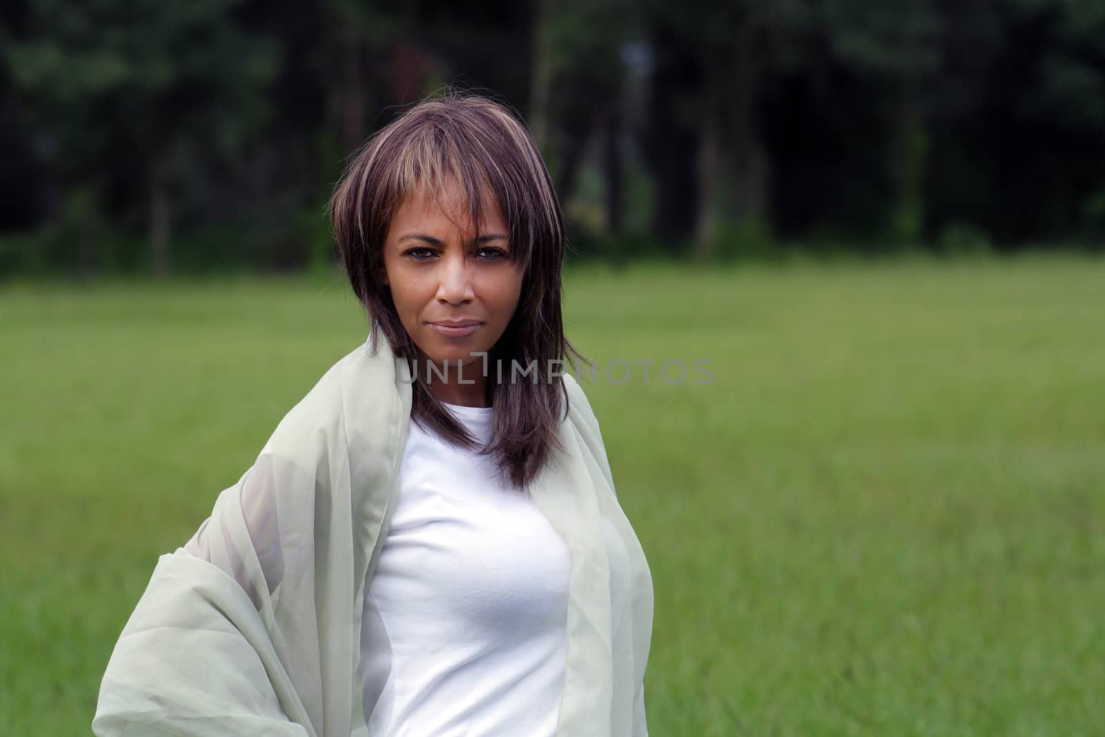 A beautiful mature black woman soaks up some atmosphere with a swatch of sheer fabric outdoors, looking directly into the camera.