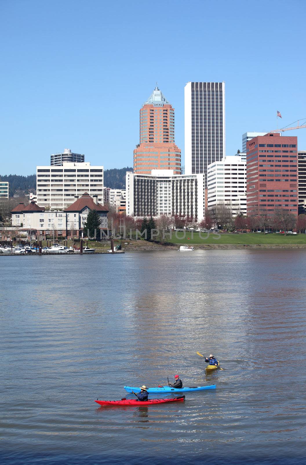 Three kayaks on the Willamette river enjoying the spring weather with the city on the background.