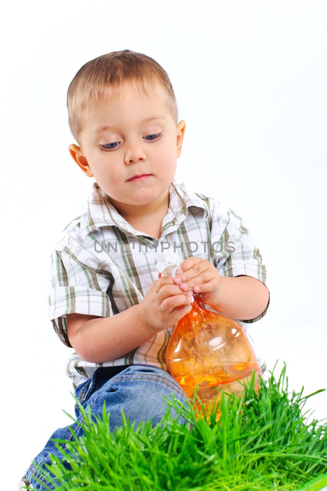 Cute boy watering the green grass. In the studio