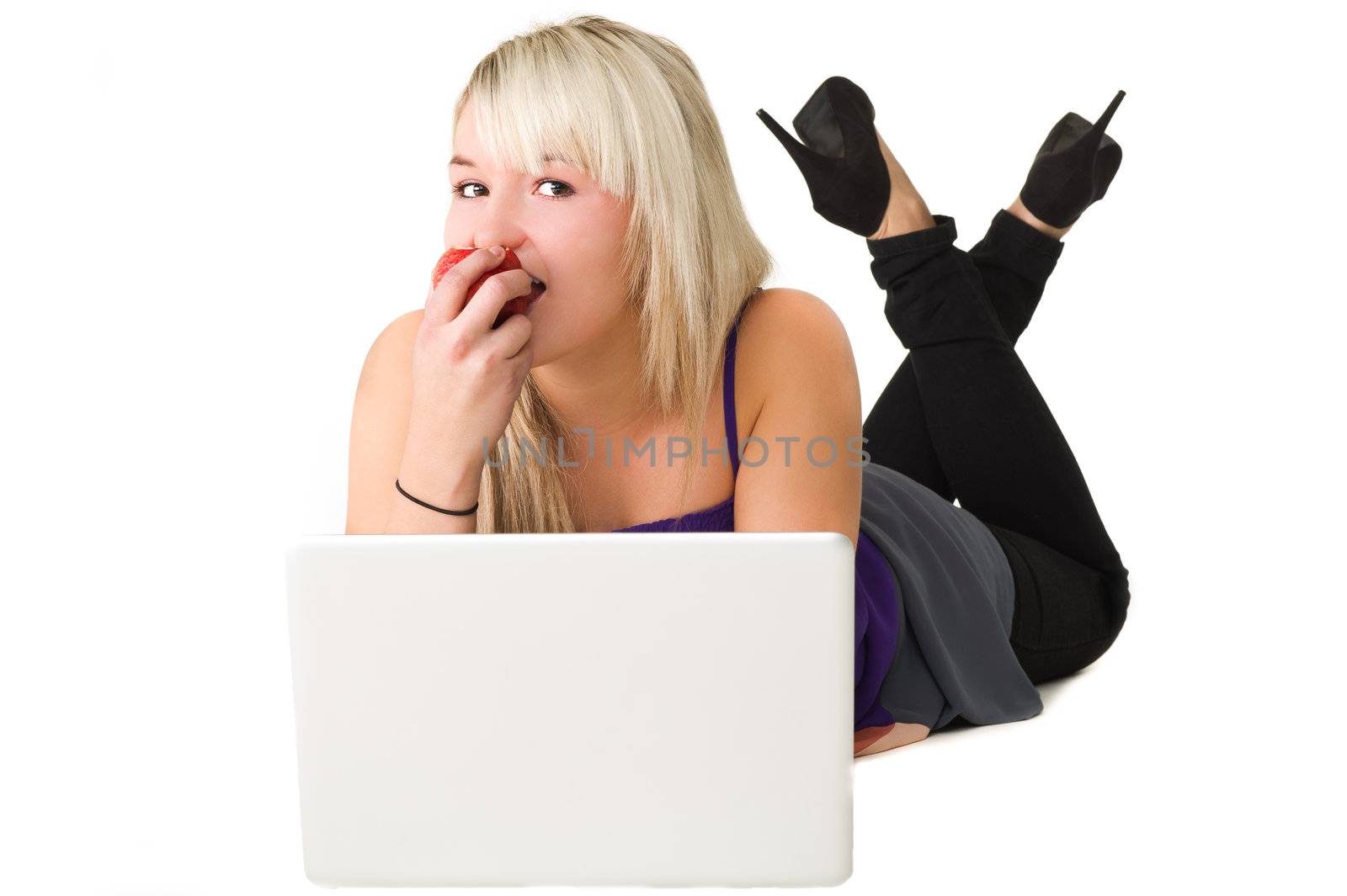 Young beautiful girl using here laptop while eating an apple. Over white background