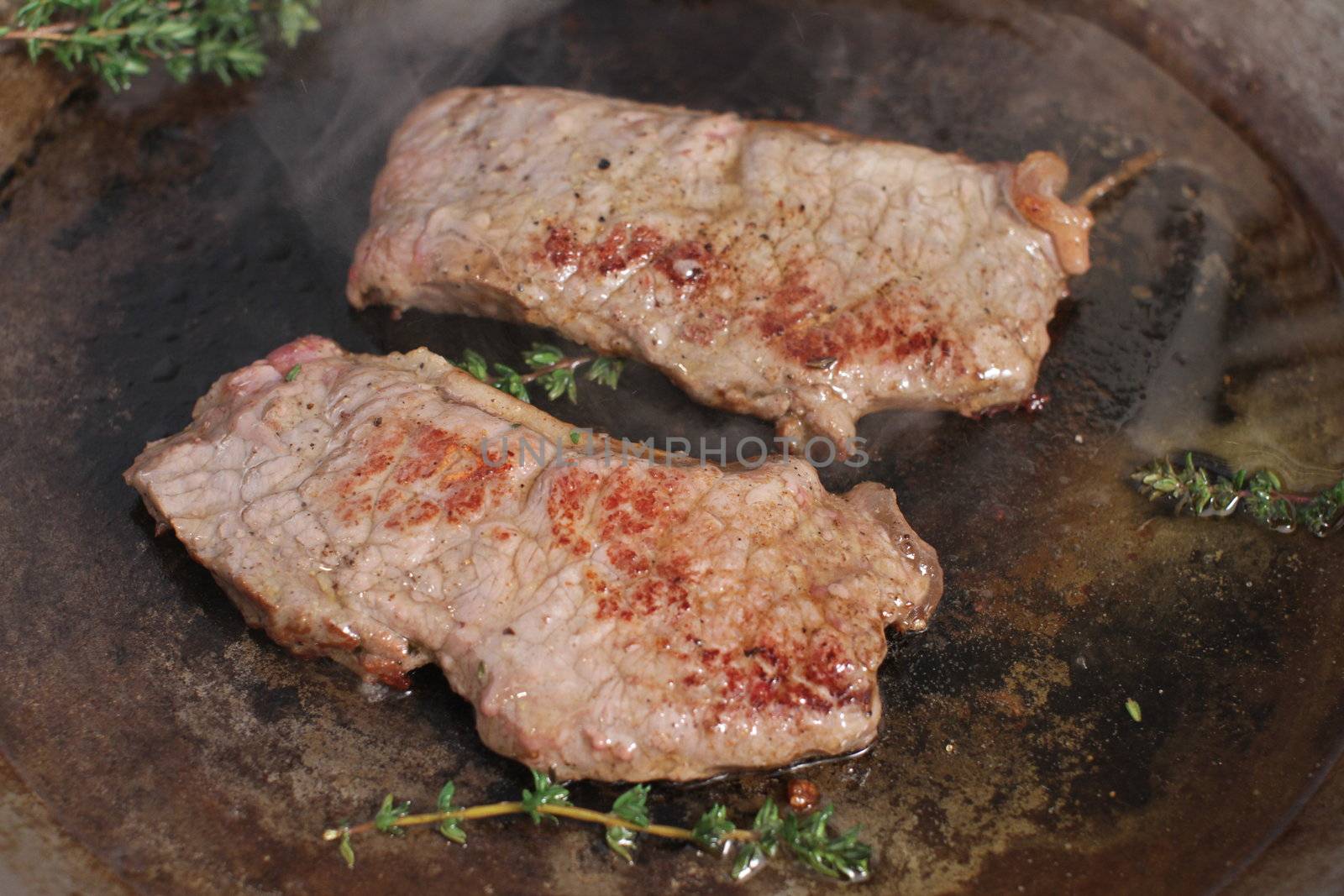 Beef steak cooking in a iron grill pan.