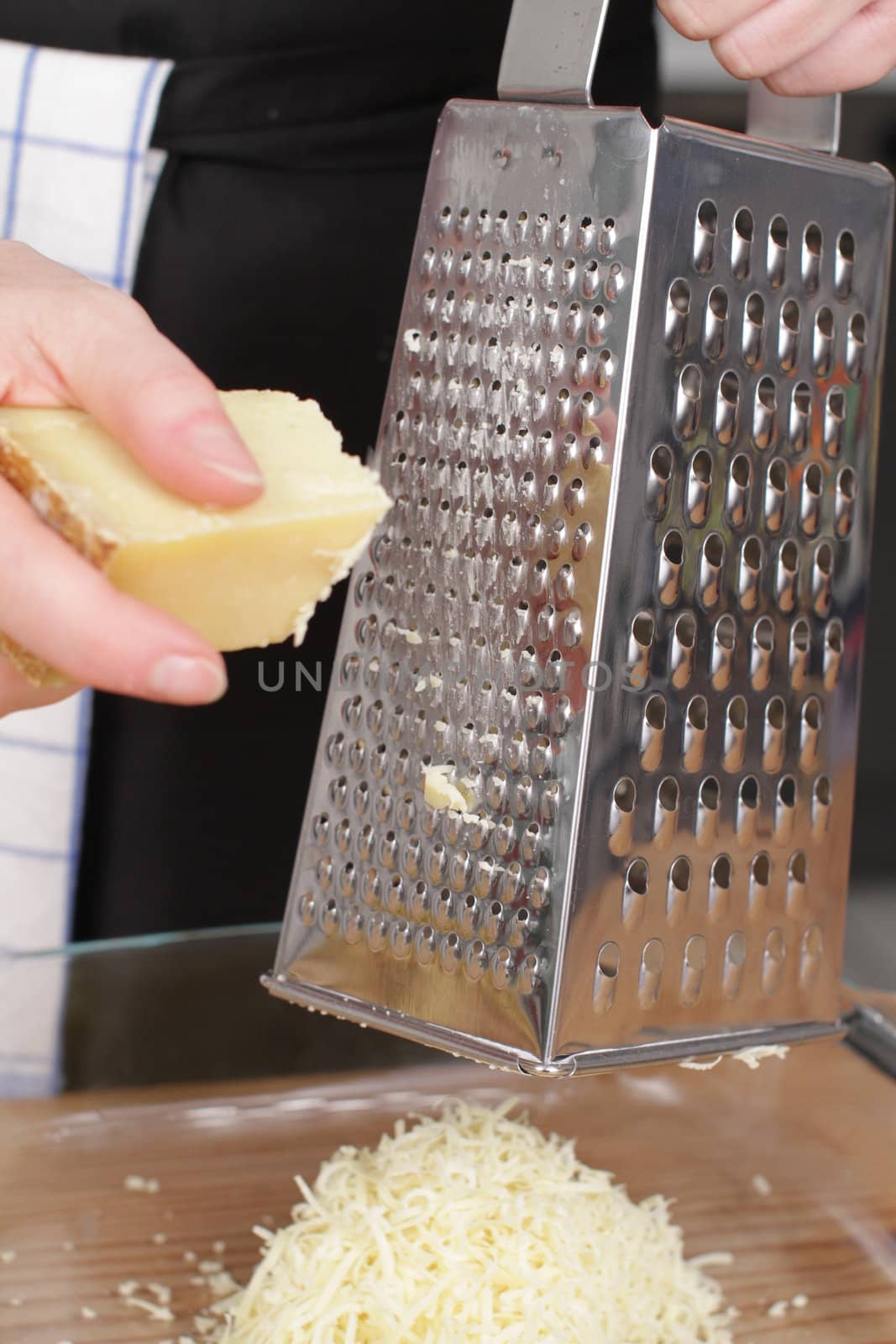 Parmesan cheese with grater on wooden chopping board.