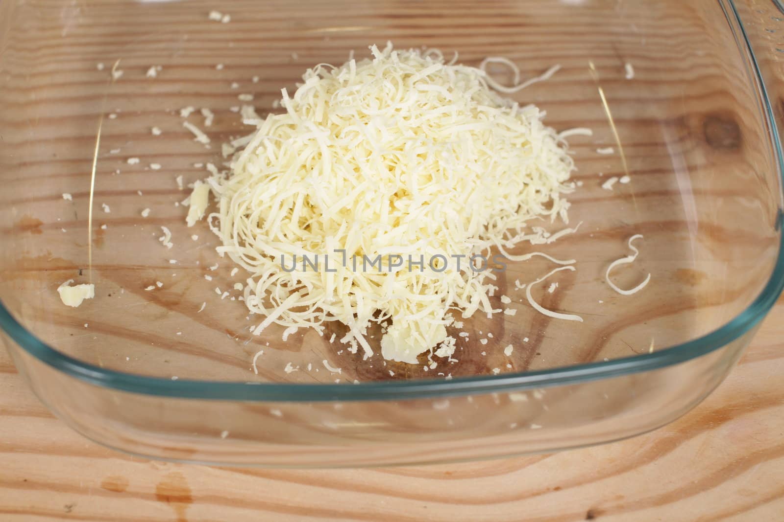 Parmesan cheese with grater on wooden chopping board.