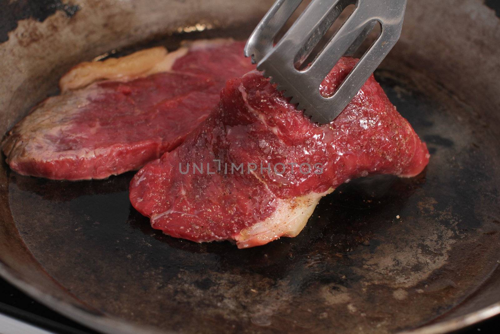 Beef steak cooking in a iron grill pan.