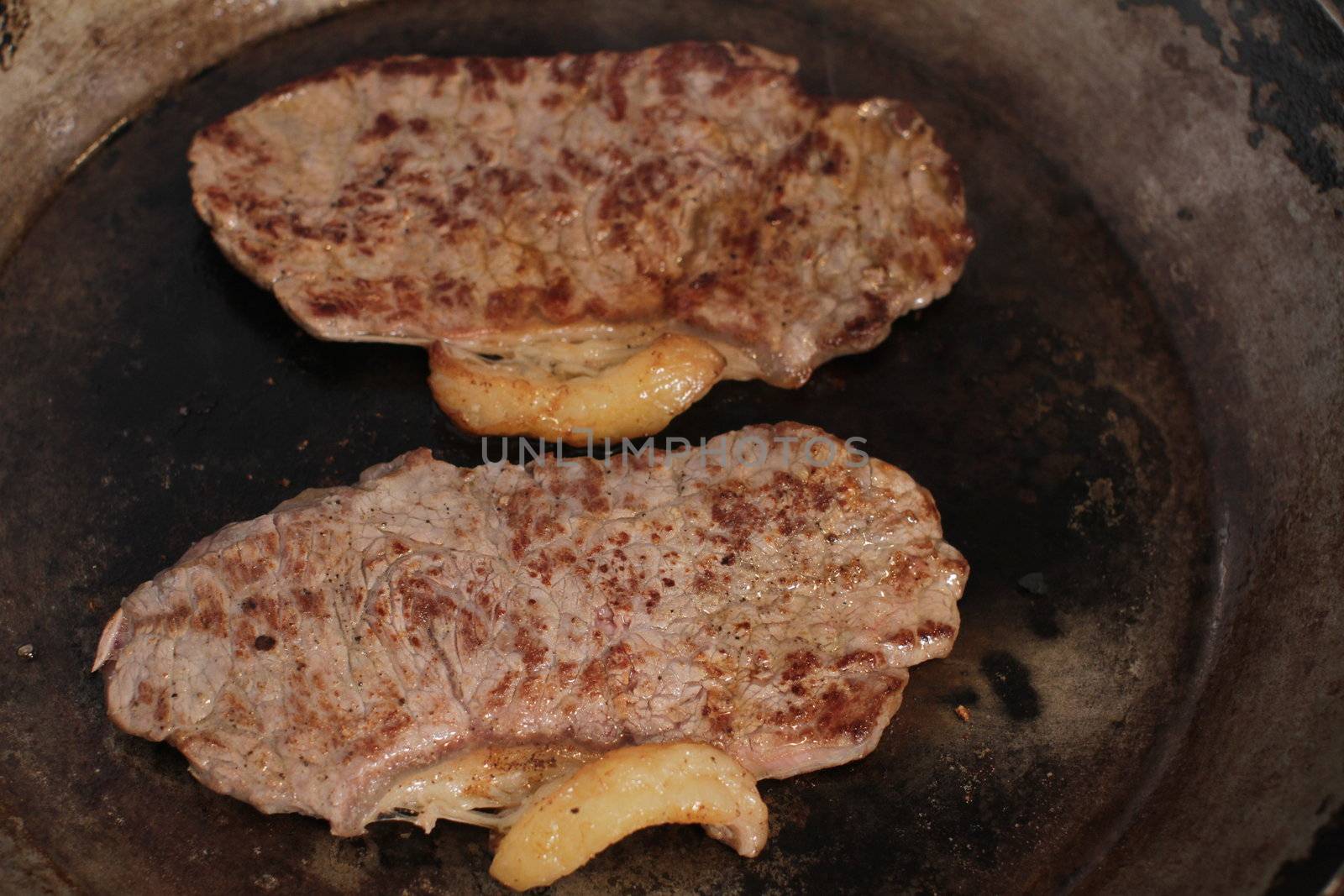 Beef steak cooking in a iron grill pan.