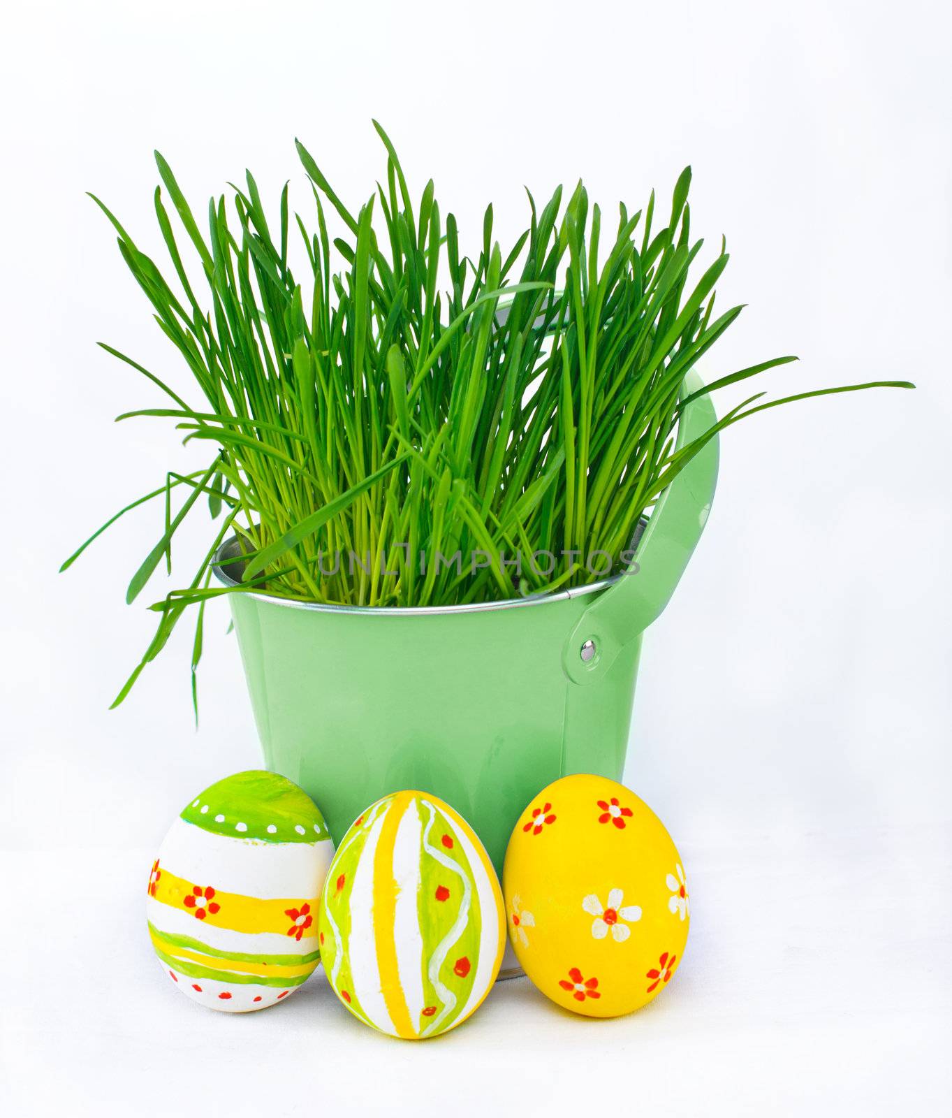 Easter eggs next to the bucket with the green spring grass