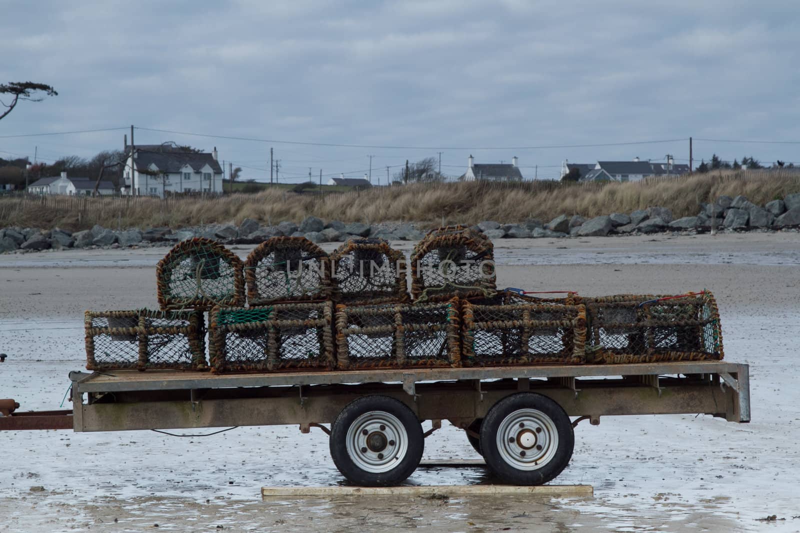 Lobster / crab pots stacked on a trailer on a beach with supporting planks under the tires.