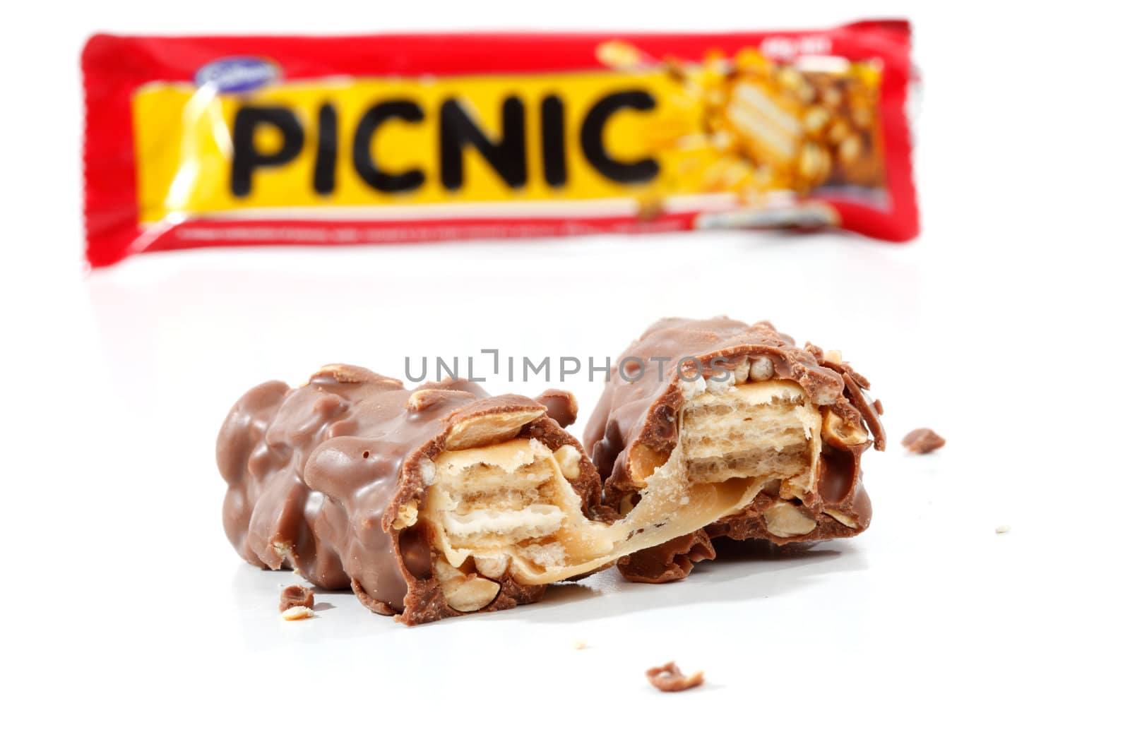 A Cadbury Picnic chocolate bar 46g (1021kj).  Showing wrapper packaging in background and chocolate bar contents in focus in the foreground. Picnic contains nuts, wafer, chocolate, rice crisps and caramel.  Photographed in studio on a white background.