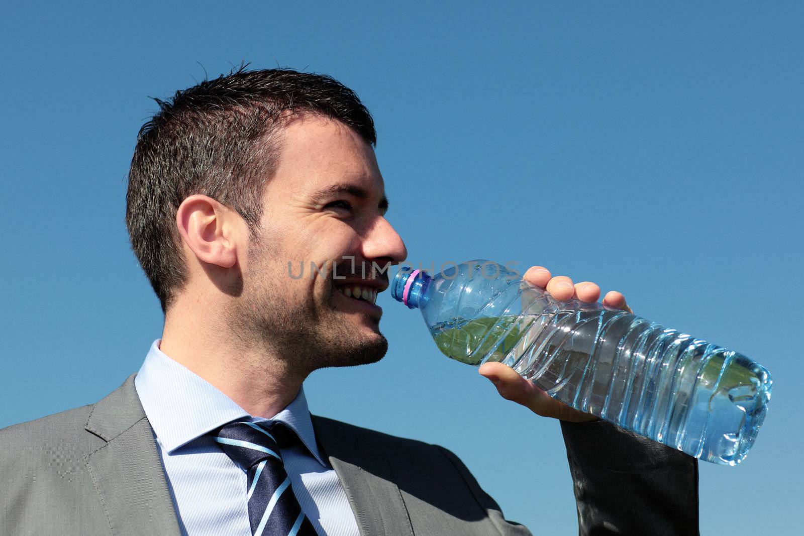 handsome businessman drinking water with bottle in blue sky
