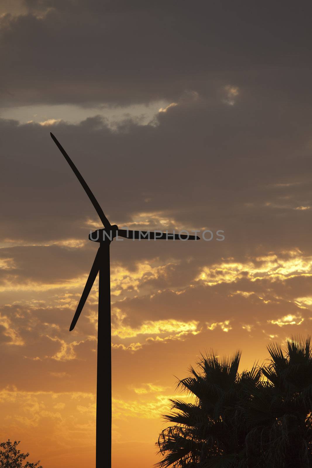 Silhouetted Wind Turbine Over Dramatic Sunset Sky and Clouds.