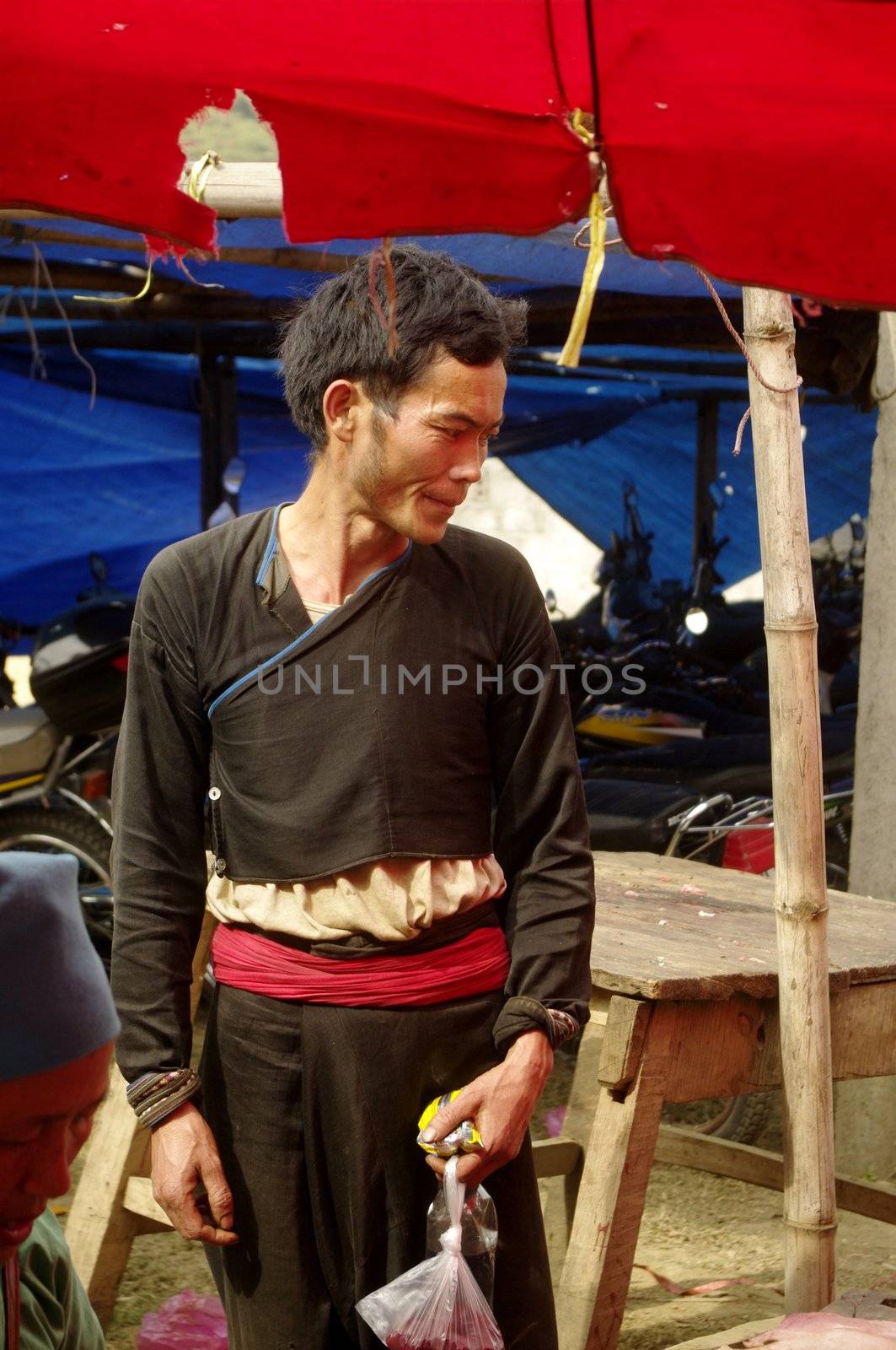 Man of the Red Dao ethnic group in Muong Hum market. North Vietnam. Costume rare on a man because only women have kept the tradition. Jacket and baggy black and red fabric belt