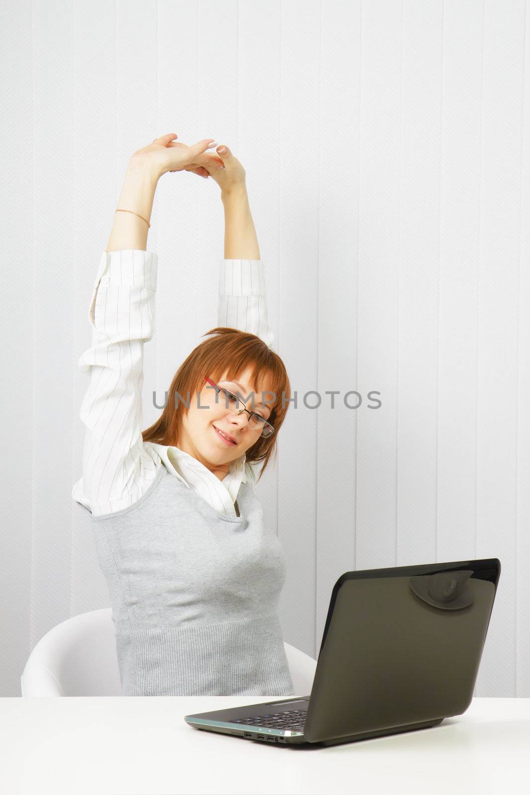 tired girl with a laptop stretches in the workplace