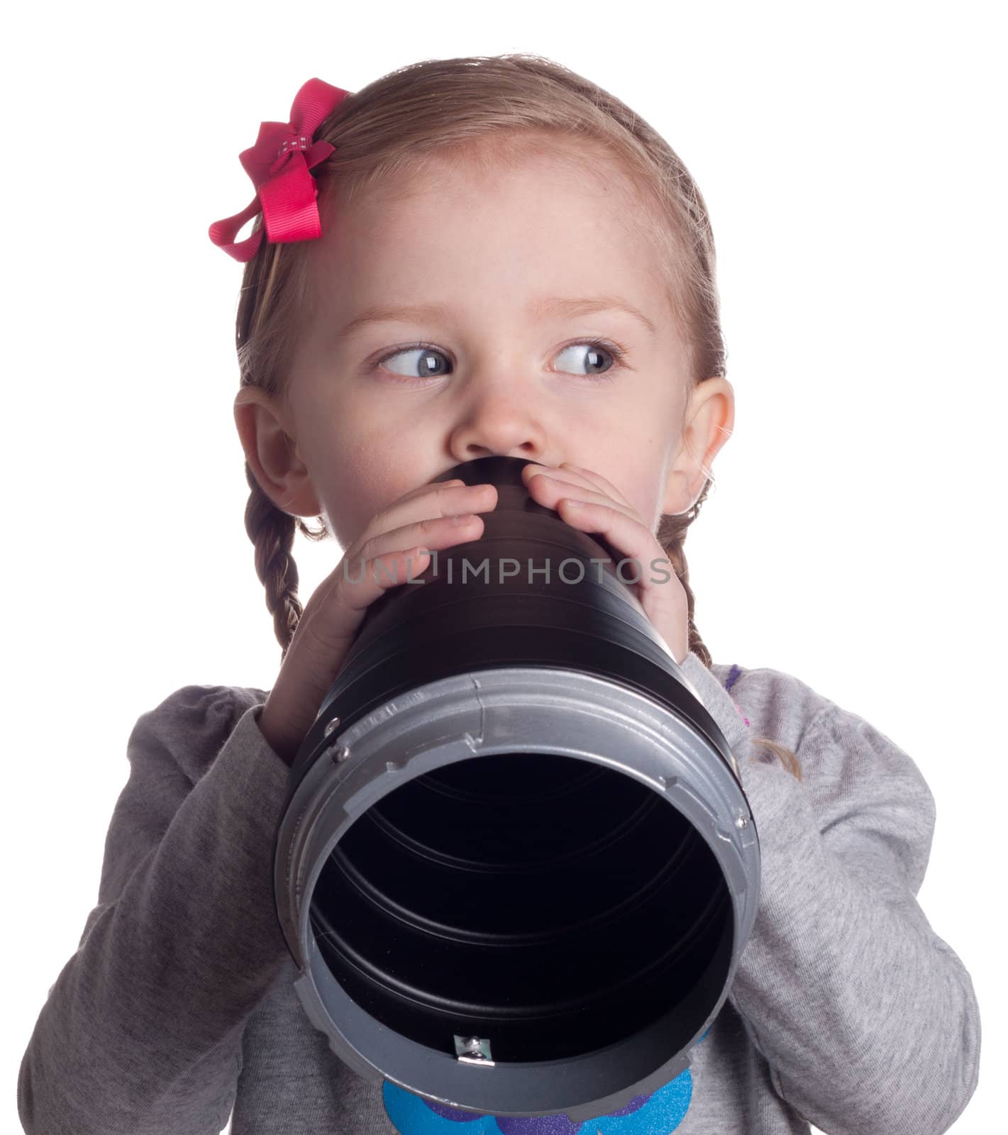 A very serious young child is talking secretly into her pretend microphone.  She is keeping an eye on someone so they do not see her.