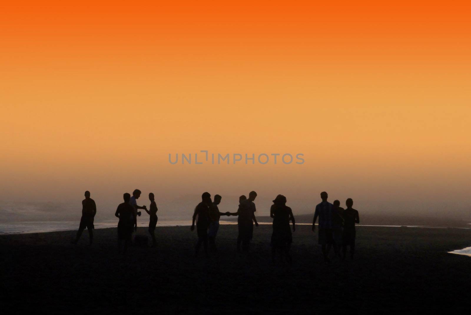 Silhouetted people socializing at the beach under orange sunset. 