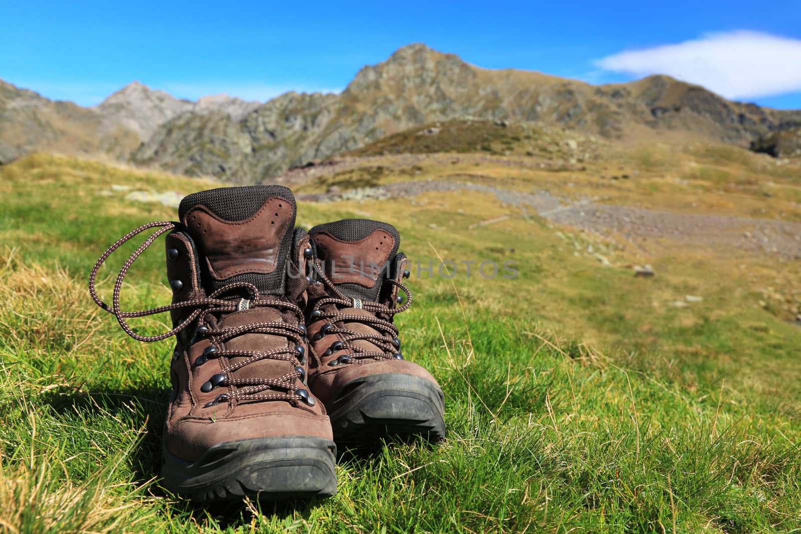 Image of a pair of hiking boots lying in the grass in front of a beautiful mountainous landscape in Pyrenees Mountains.