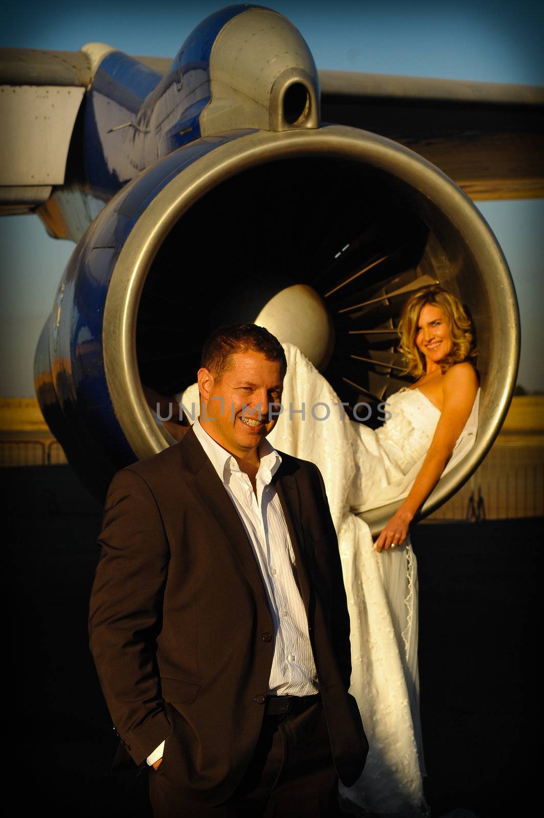 sexy young adult wedding couple laying inside the engine intake of Boeing passenger aircraft with groom infront