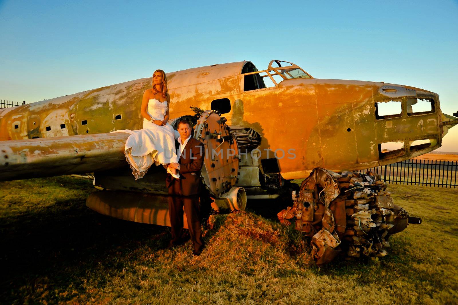 young wedding couple standing at crashed old Dakota war plane by Ansunette