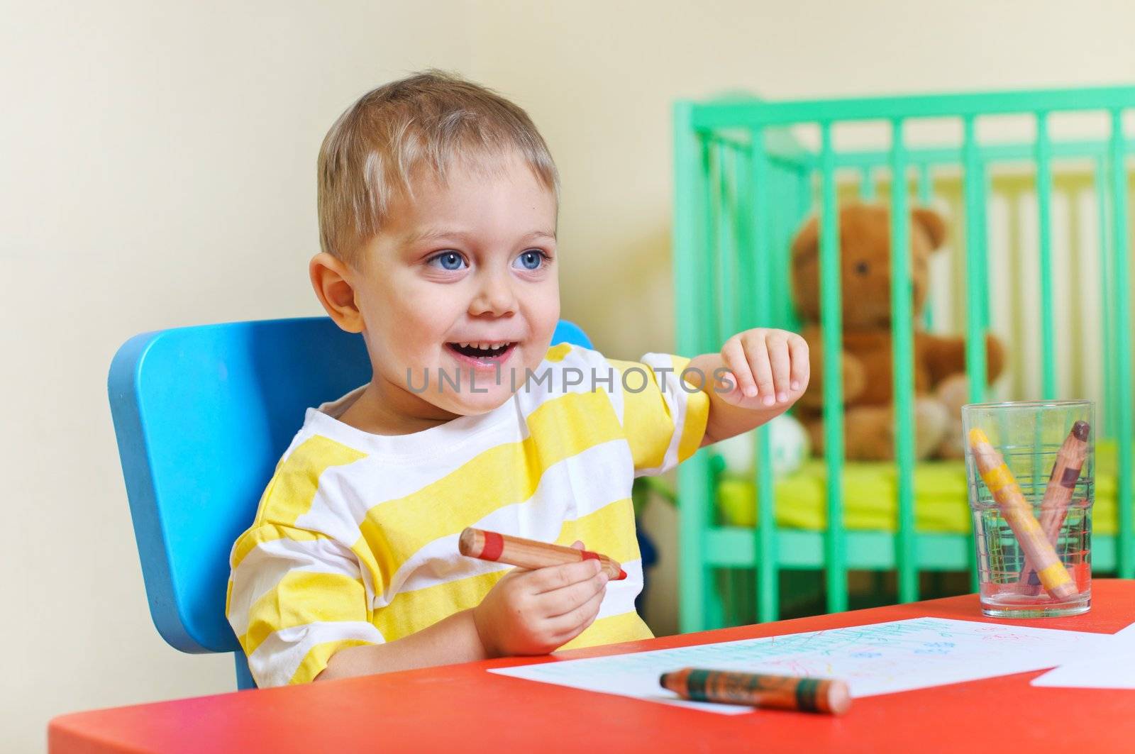 Little cute boy draws with crayons in the nursery by maxoliki