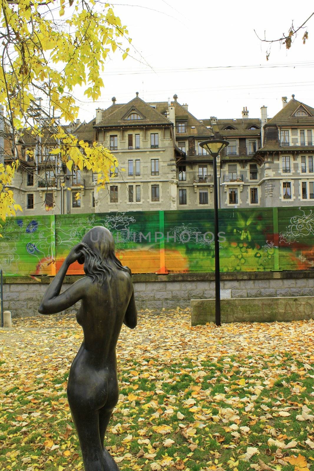 City park with yellow leaves, a statue, graffities and buildings by autumn weather