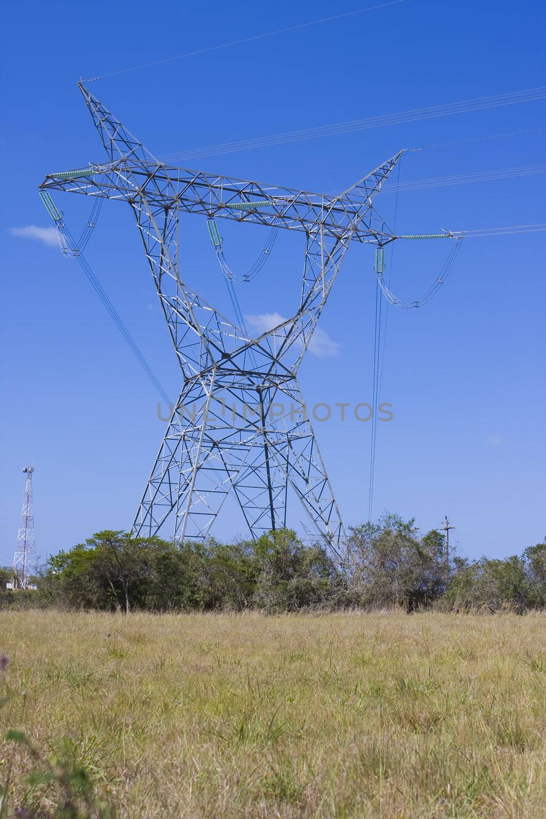 Electrical tower standing in the fields with communication tower behind
