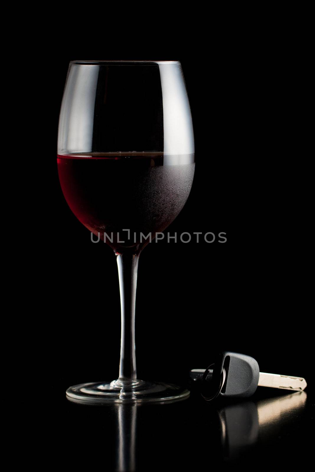 Glass of red wine and car keys on a table or bar.
