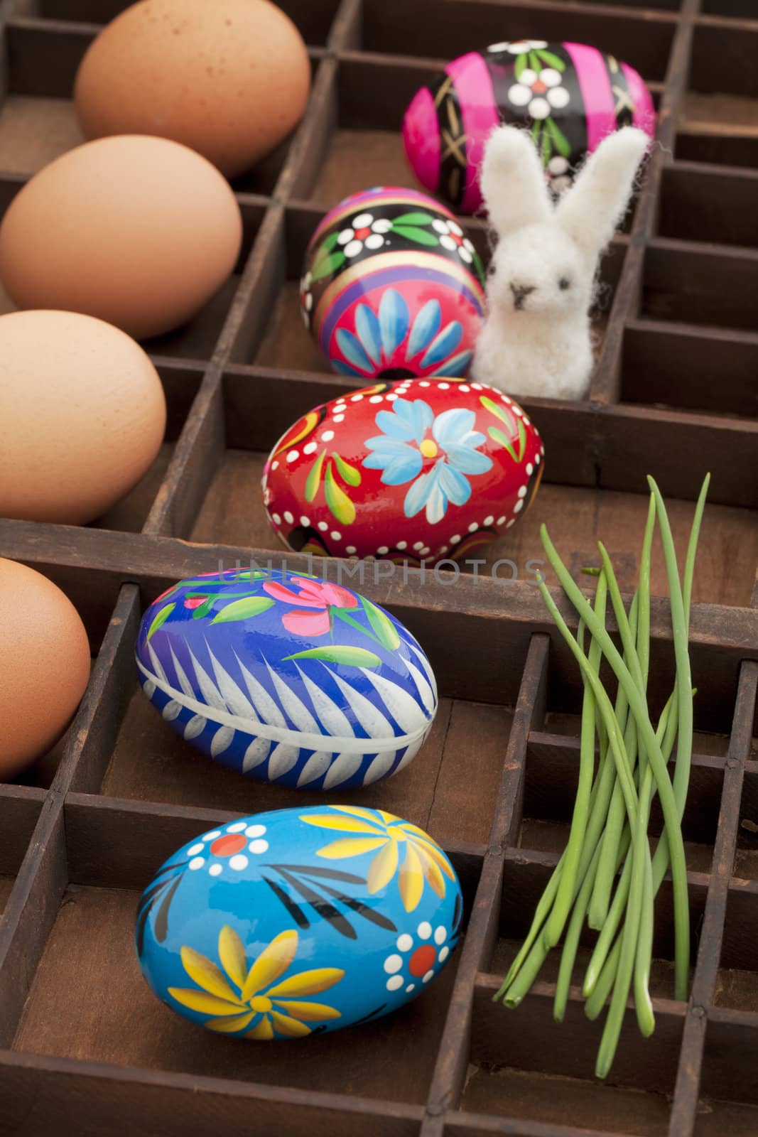 Easter decoration concept - brown chicken eggs, painted eggs with floral motif, green chive and woolen bunny in a vintage drawer (shadow box)