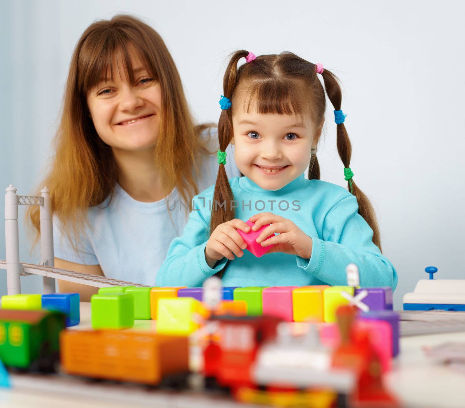 Mother and daughter cheerfully playing with toys on blue