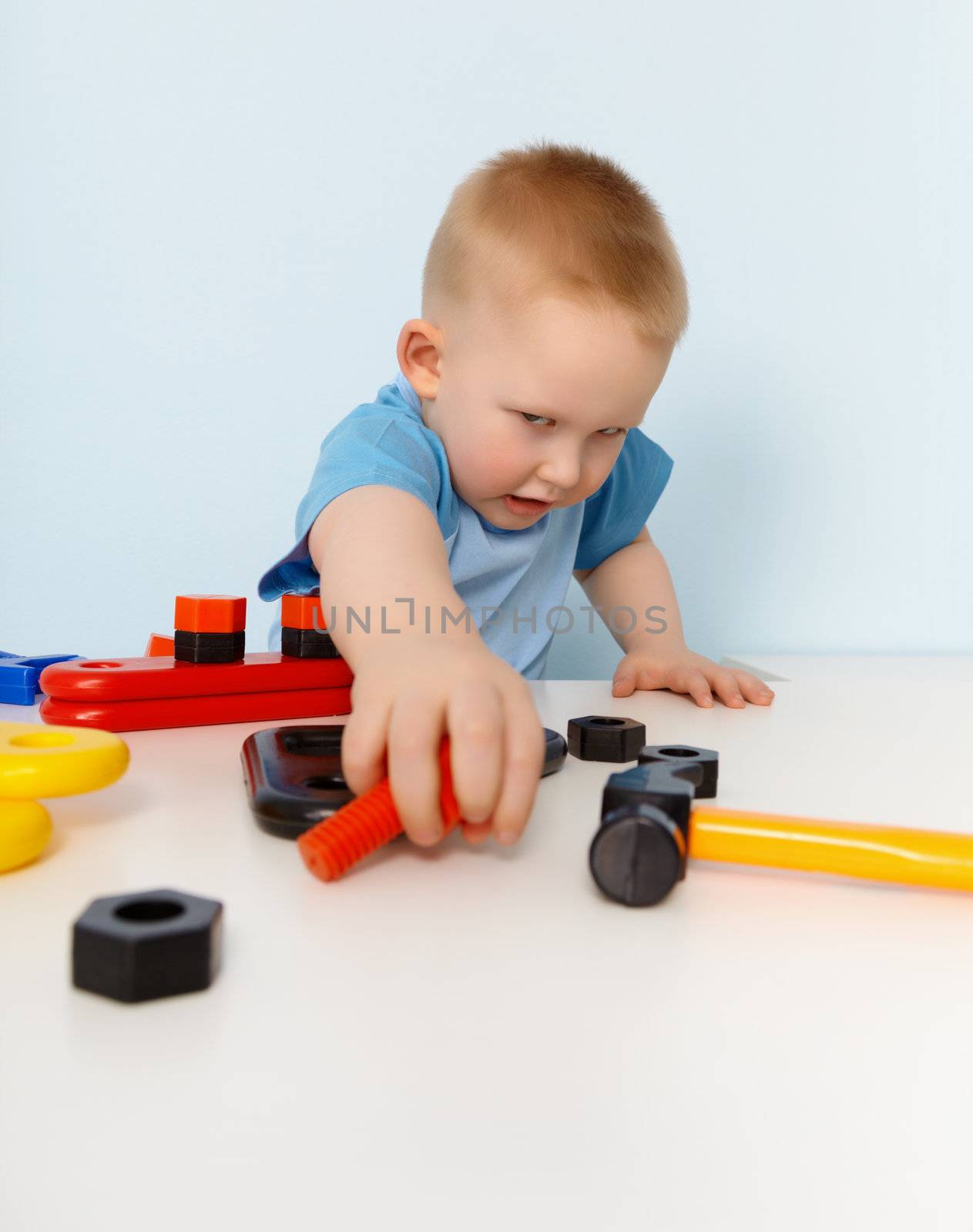 Little boy playing with a toy plastic constructor on blue background