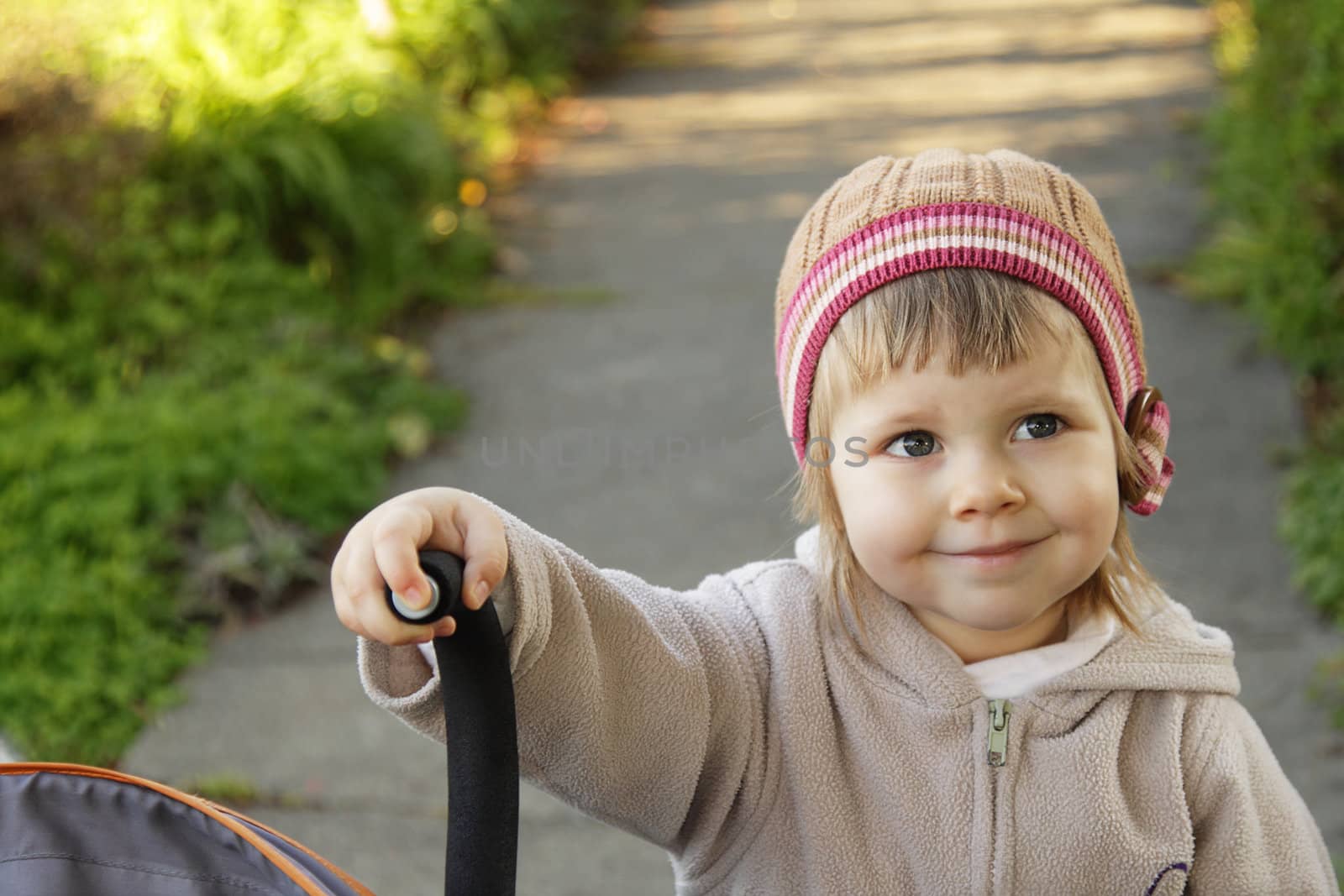 Cute toddler girl with a hat by the stroller outdoors