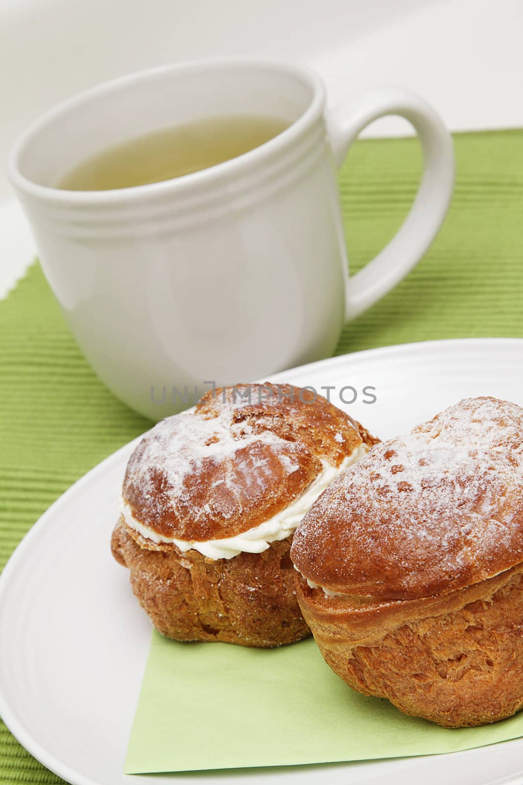 Two profiteroles on white plate and a cup of green tea