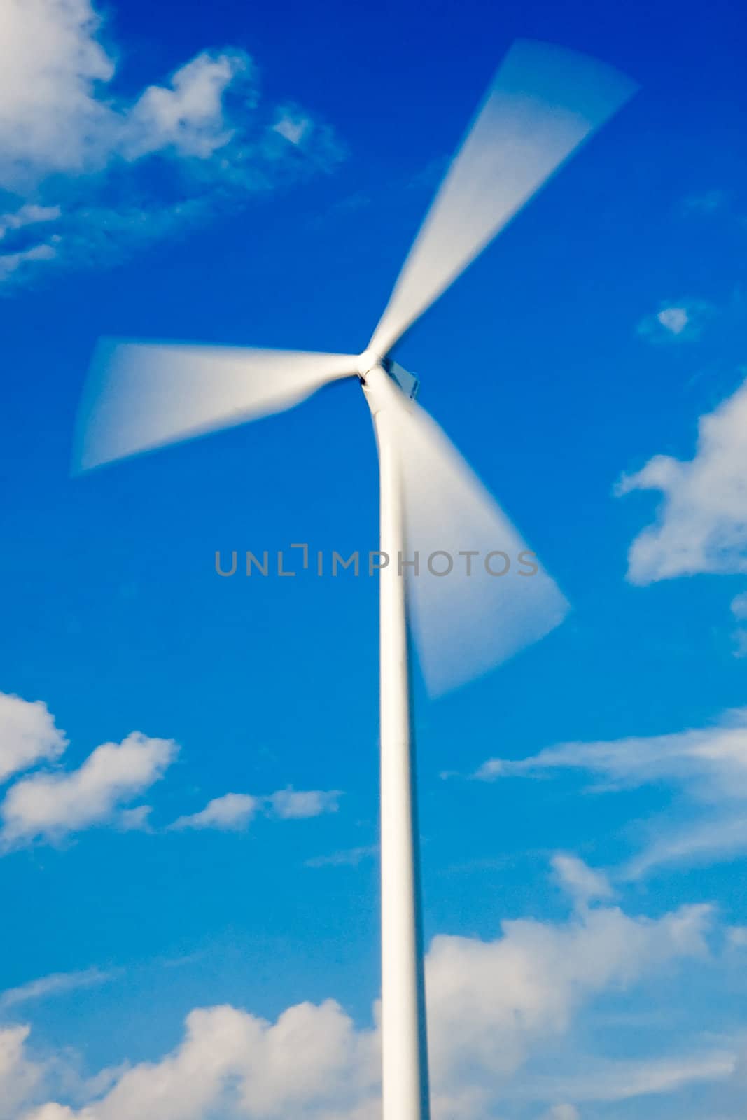 Fast spinning wind turbine and blue sky with few clouds (rotor with strong motion blur)