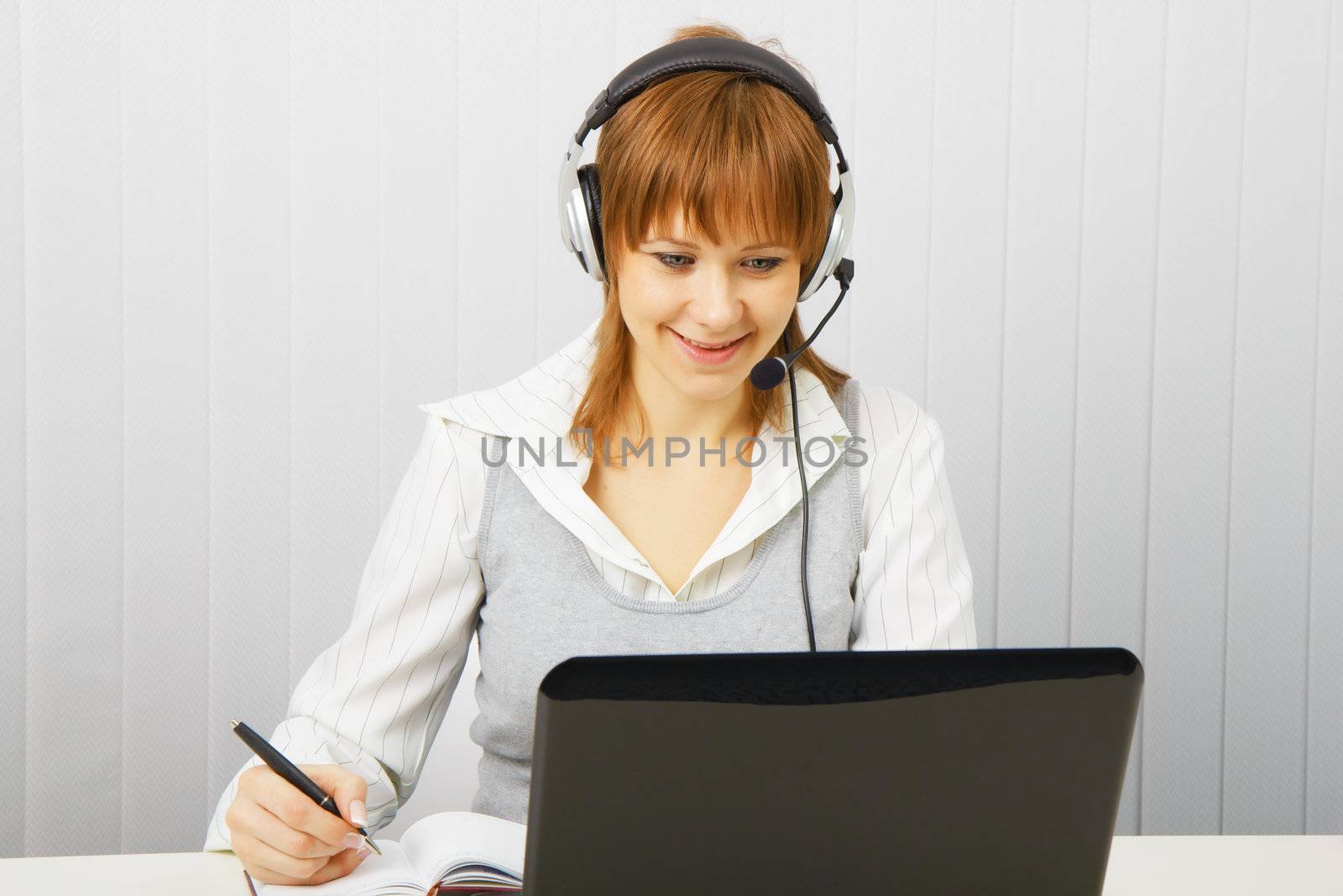 Attractive girl in a white blouse with a laptop in headphones with microphone
