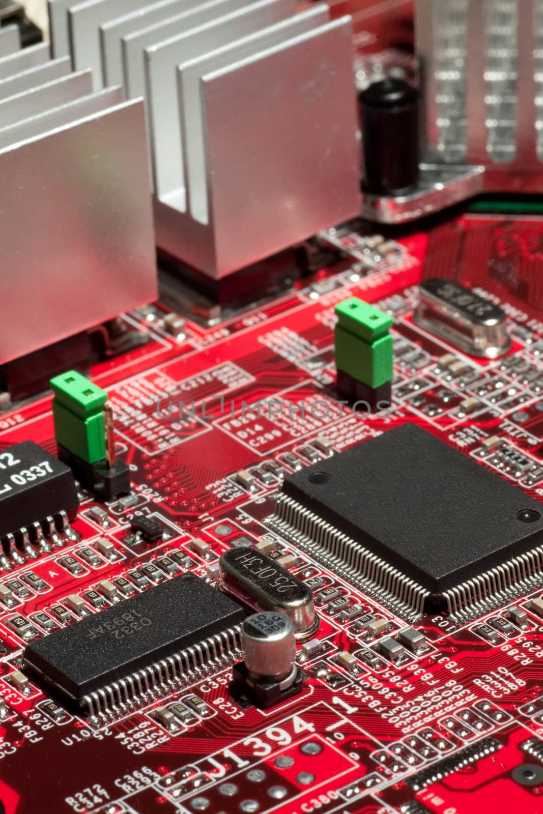 Red circuit board with electronic components such as microchips, condensors, resistors, and transistors.