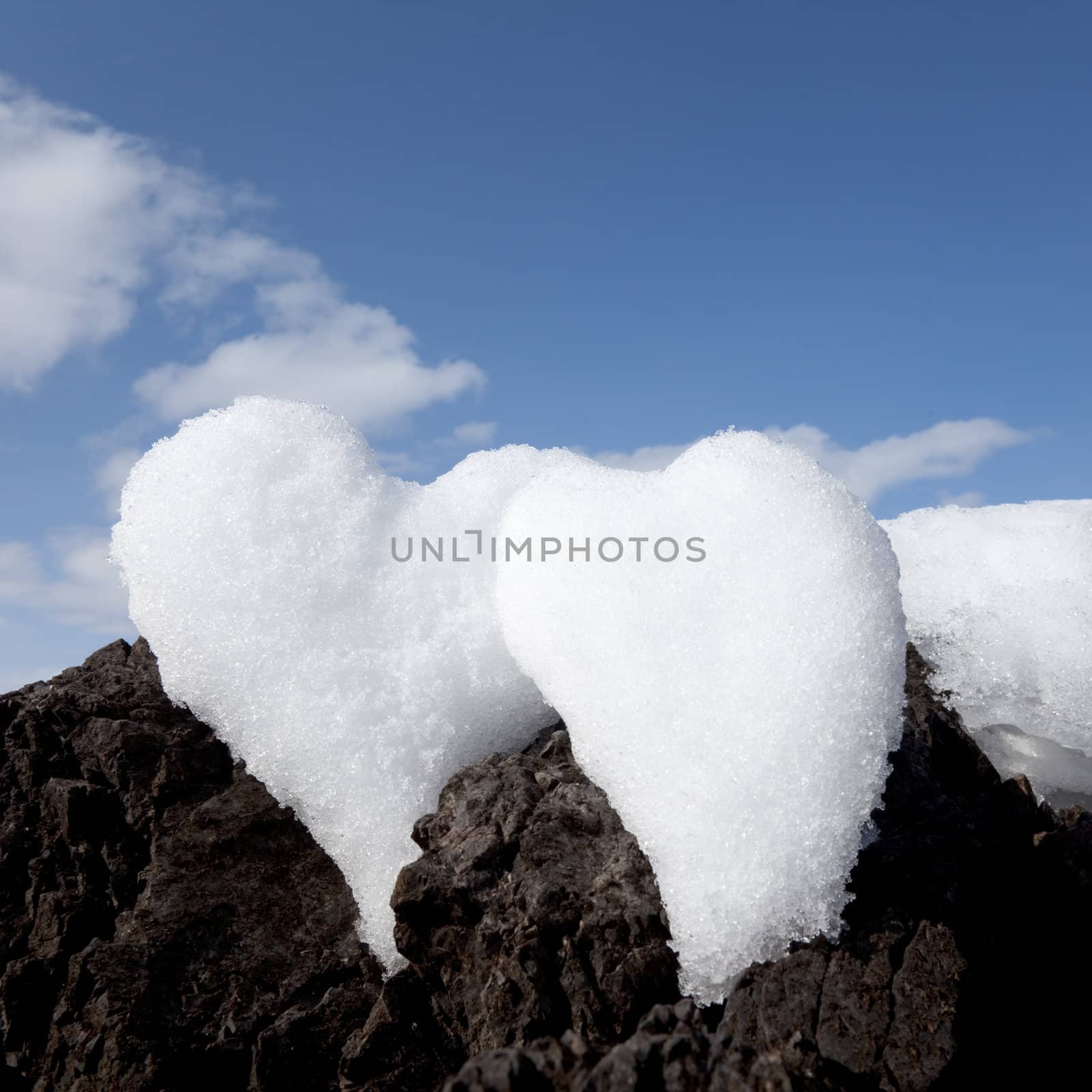 Two Valentine�s Day Hearts formed from snow on rock with blue sky.