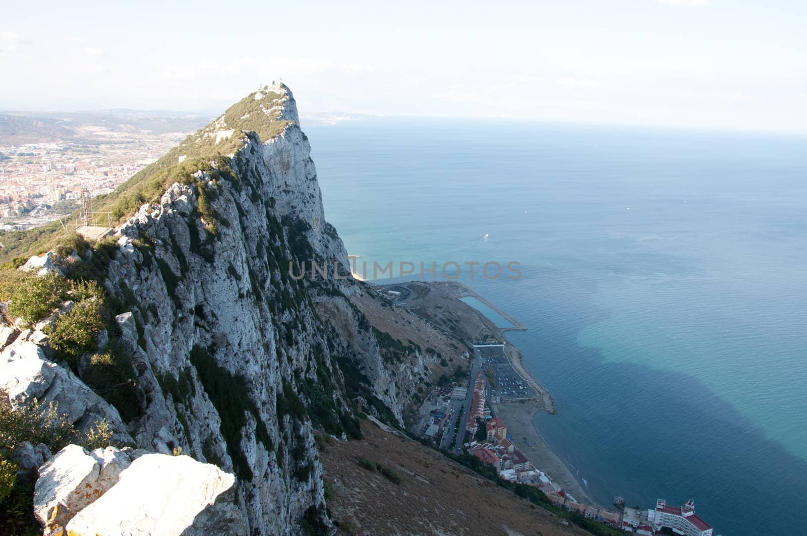 Steep rocky coastal lookout point ridge and cliffs overlooking ocean with a city in the distance.