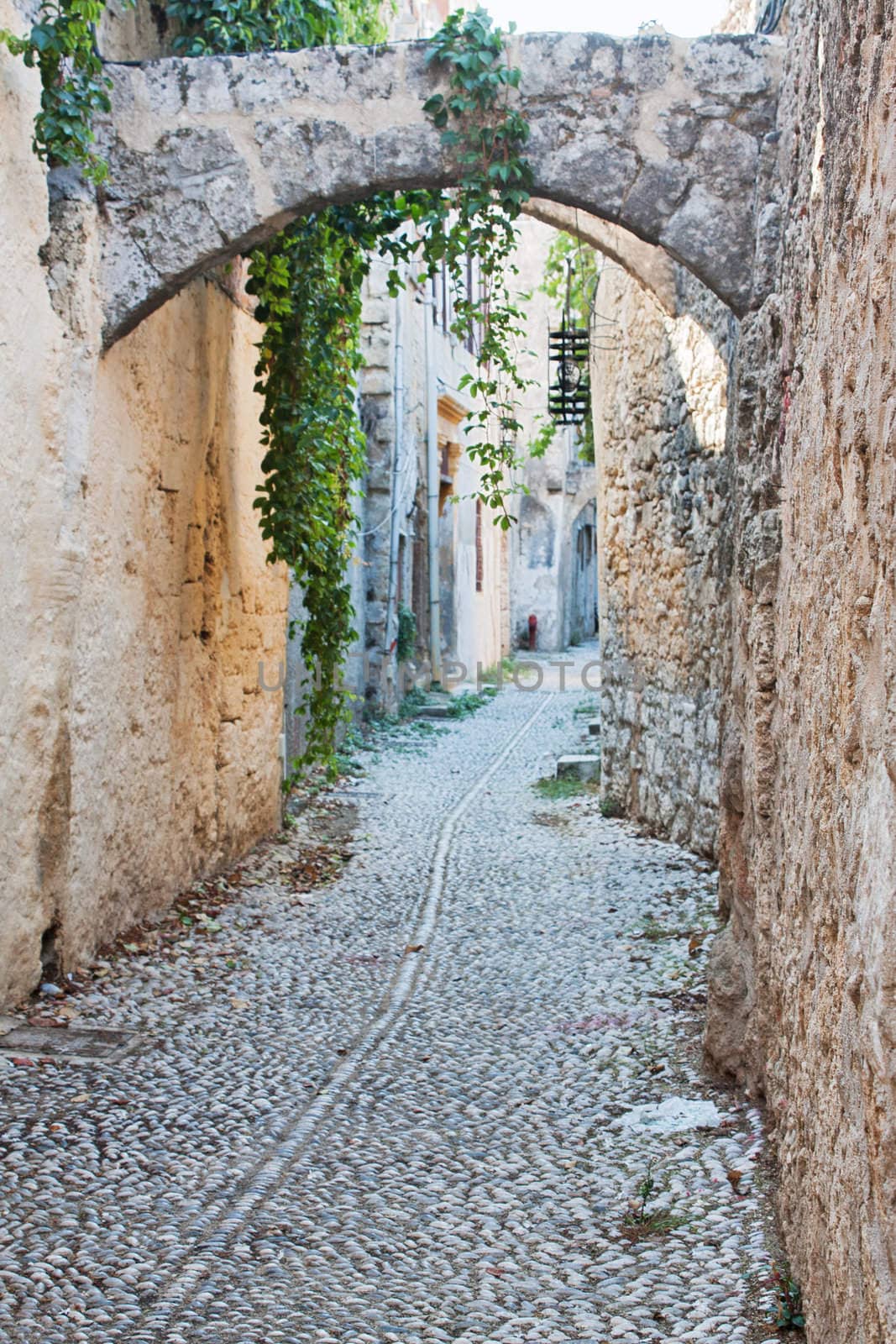 A medieval cobblestone alley in Rhodes Old Town (a UNESCO World Heritage Site), Greece, with arches and stone facades.