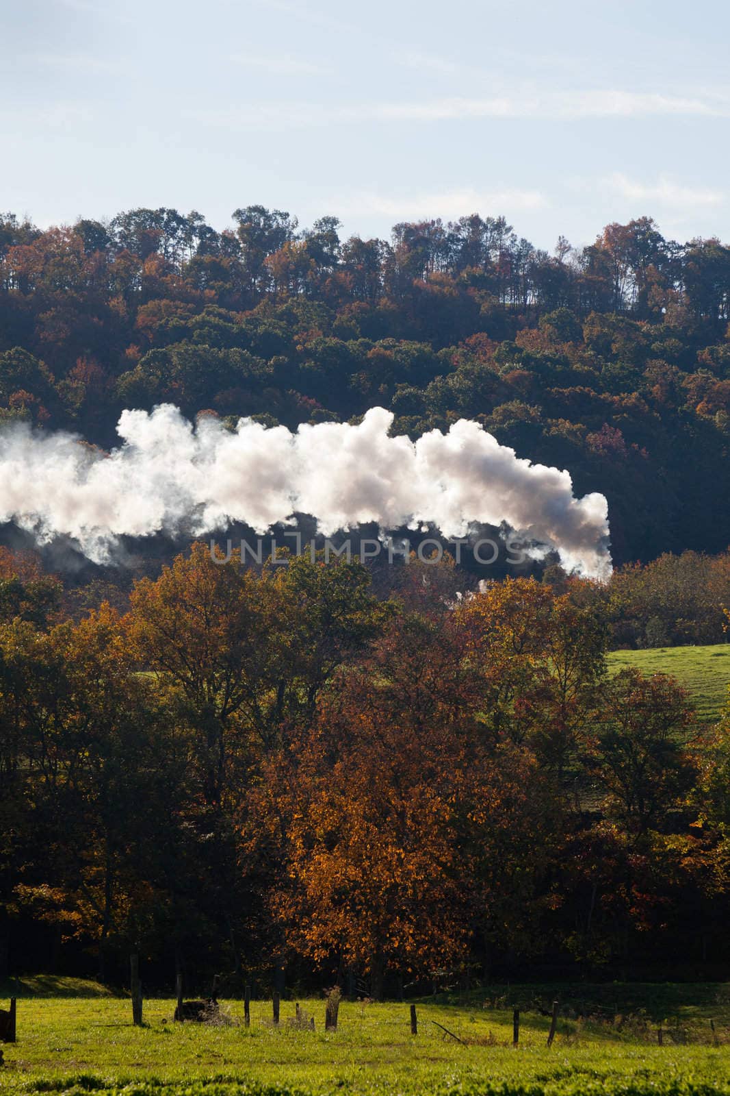 Old steam locomotive pulls freight through rural countryside in autumn