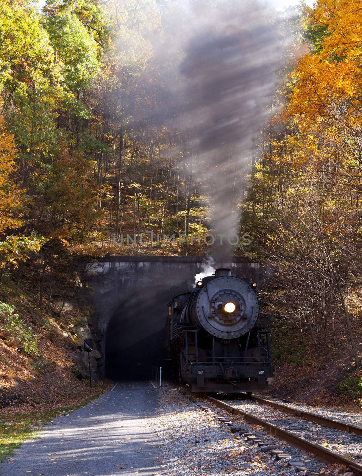 Old steam train pulling out of a tunnel belching steam and smoke