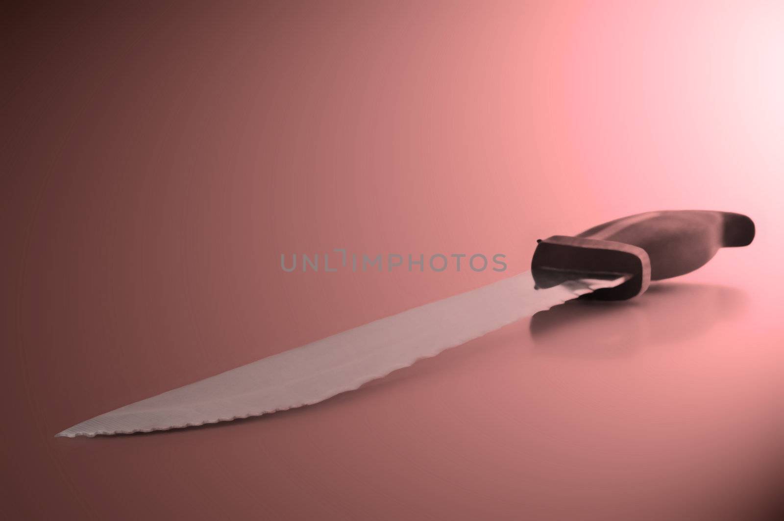 Close and low level angle capturing a stainless steel kitchen knife arranged over pink light effect filter